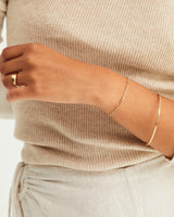 A model wearing the Anam Charm Bracelet in yellow gold, with a gold bangle and gold signet ring