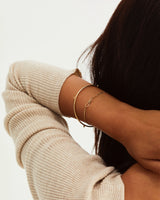 A woman wearing the Alya Bangle and the Anam Bracelet in yellow gold.
