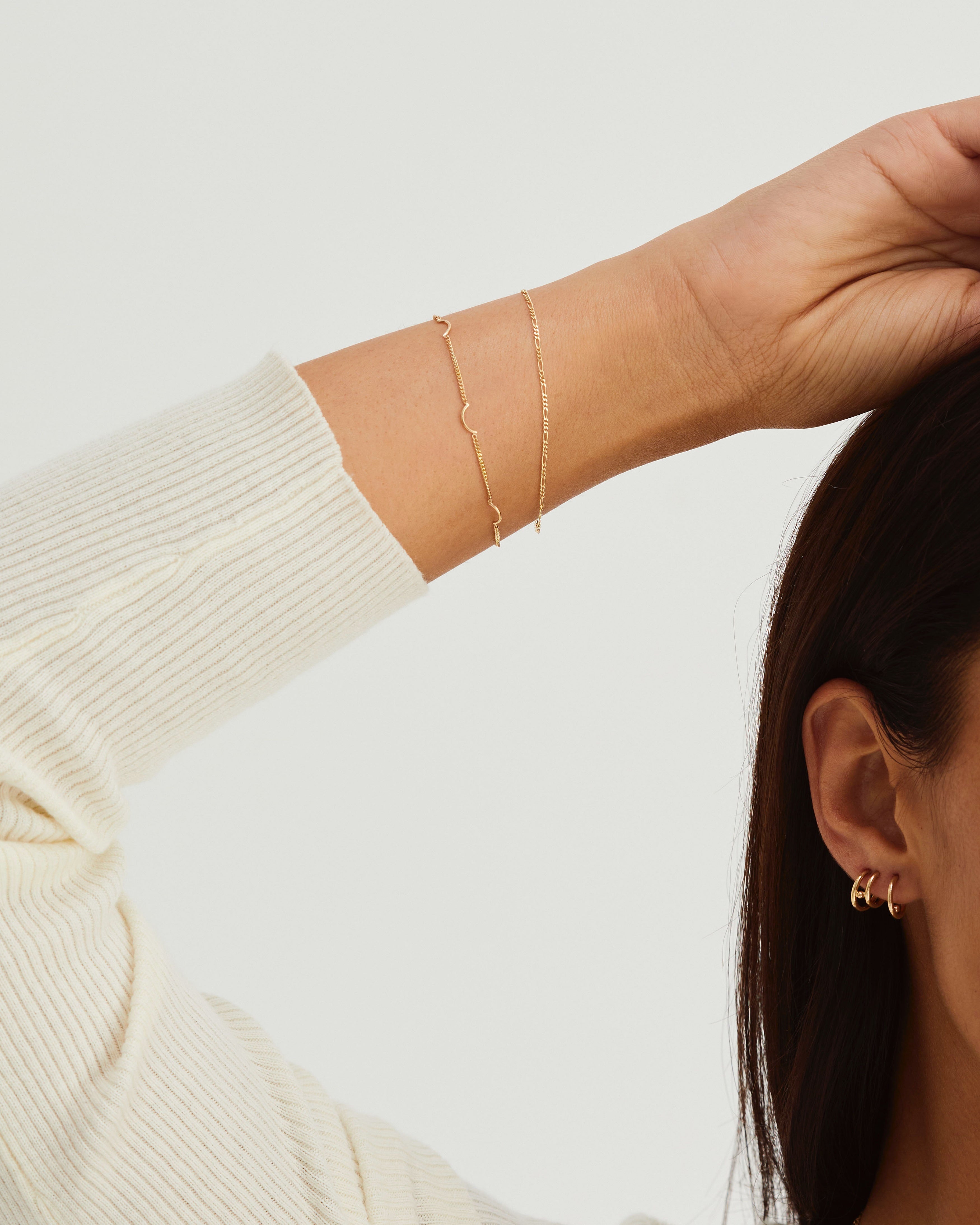 A woman wearing the Lai Bracelet and Figaro Chain, both in yellow gold.