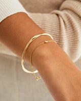 A woman wearing the Dalí Bangle and the Sonder Bracelet, both in yellow gold.