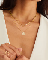 A woman layering the Golden Wattle Necklace with other yellow gold chains.