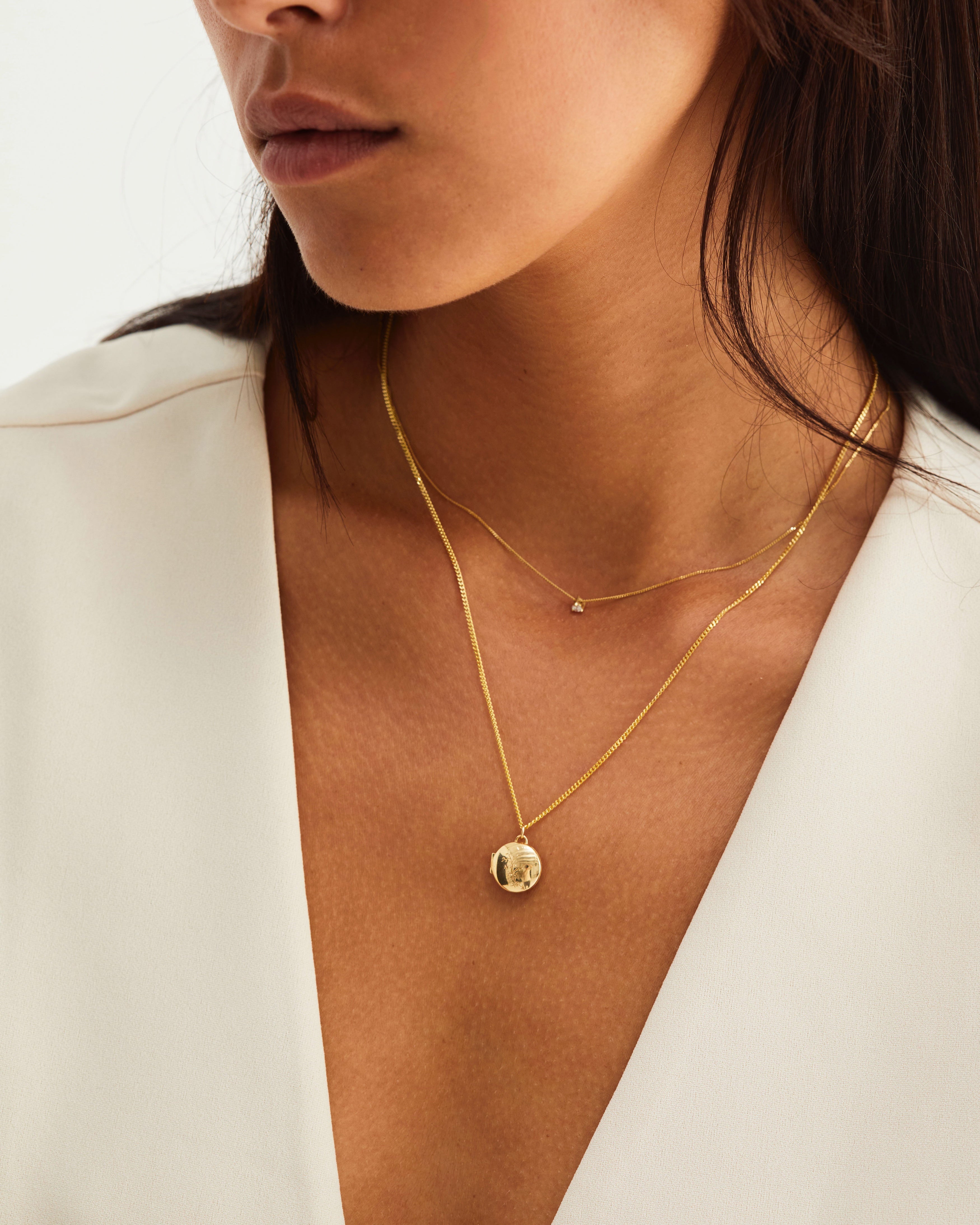 Model wears a gold locket layered with small diamond pendant