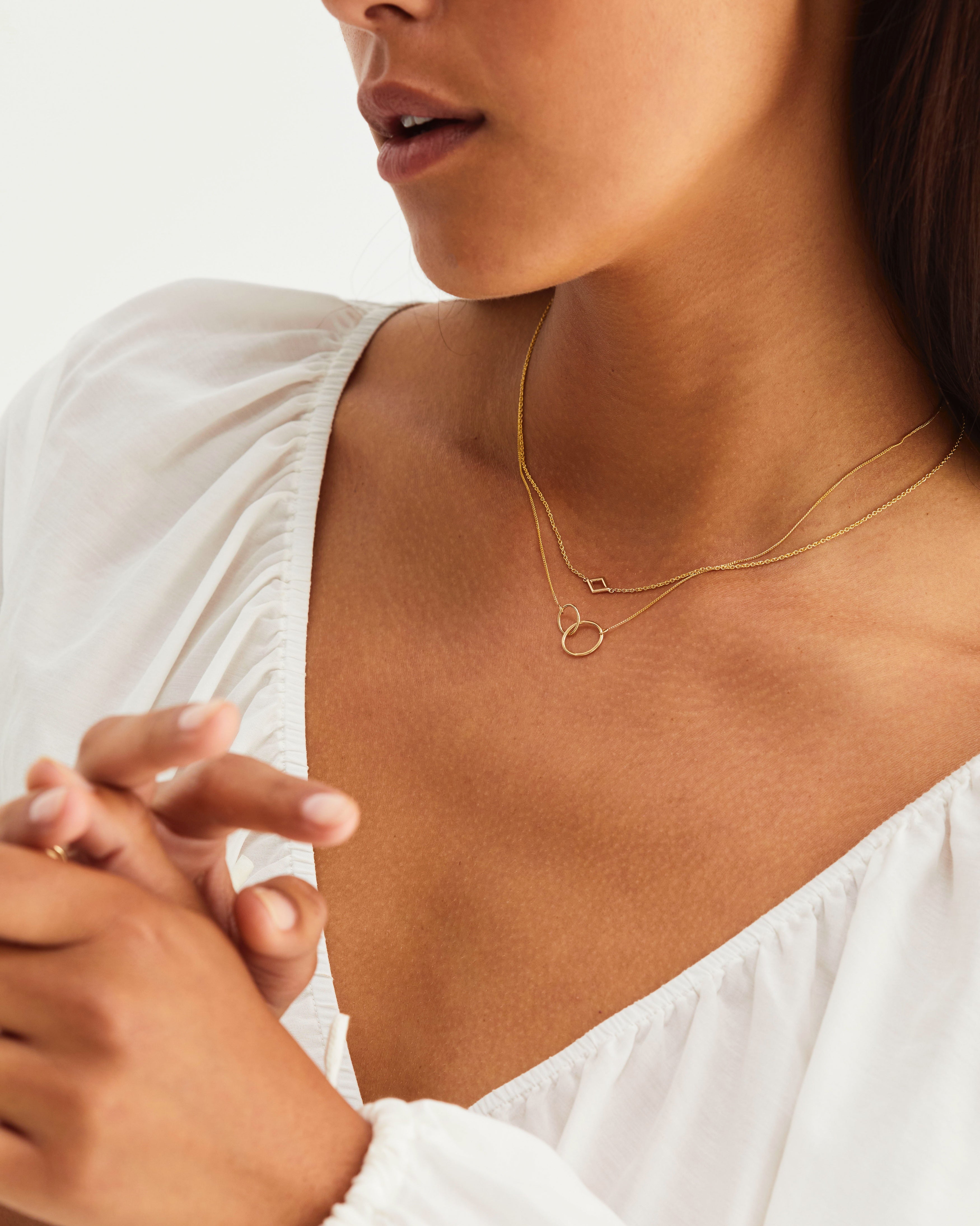A woman wearing the Loop Through Oval Necklace and the Nuna Necklace, both in yellow gold.