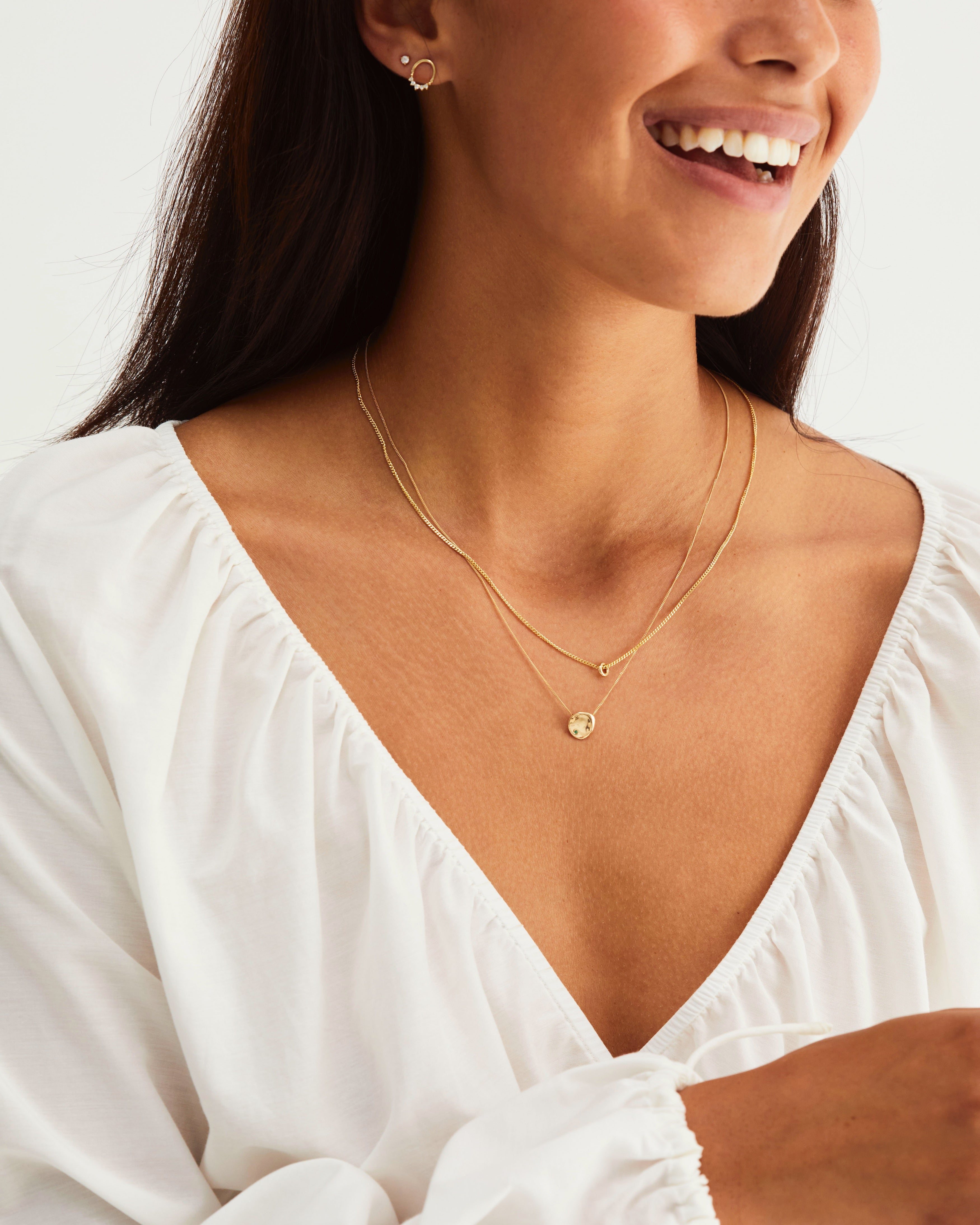 A woman wearing the Petite Mana Necklace and the Aether Necklace, both in yellow gold.