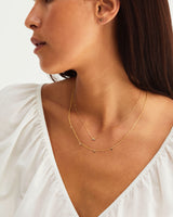 Model wears a gold chain with multiple small pendants and a sapphire pendant