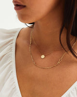 A model wears a gold initial pendant and a chain necklace featuring knots