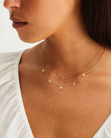 A model wears a charm necklace in yellow gold layered with a small sapphire pendant