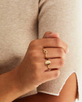 A woman wearing the Cara Ring and Mini Initial Ring in yellow gold.