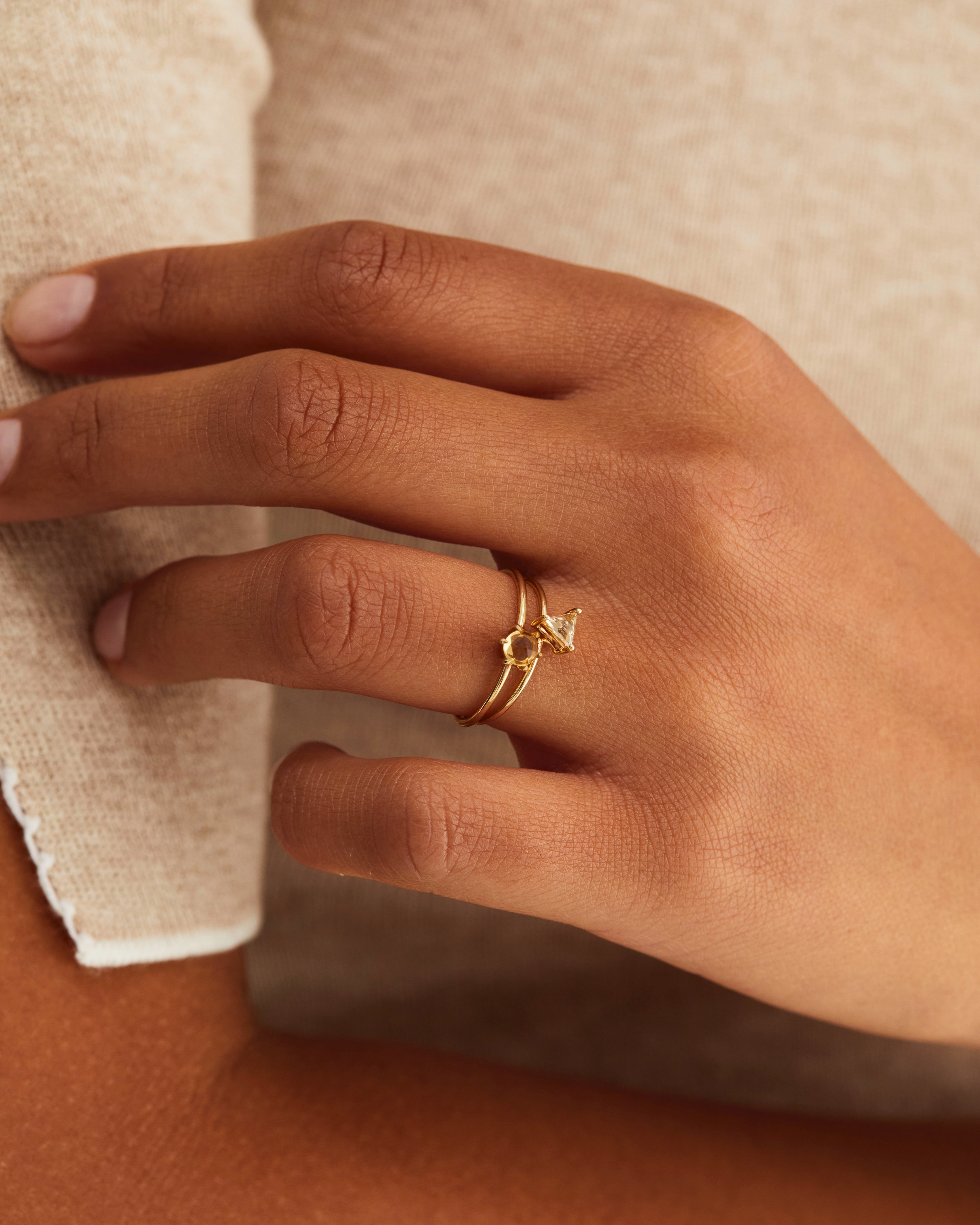 A hand adorned with the Tiny Rose Cut Ring | Honey Quartz, and the Tiny Trillion Ring | Heliodor, both in yellow gold.