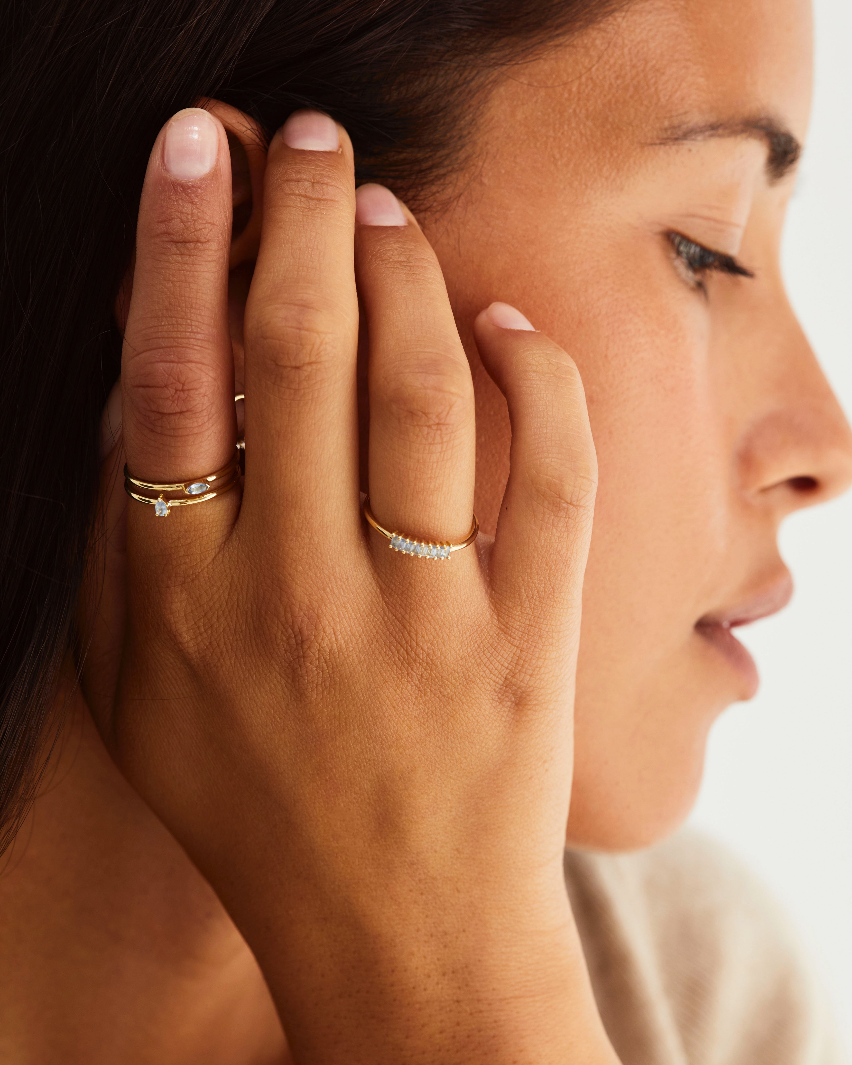 A hand adorned with the Sena Wrap Ring | Sapphire, Vega Stacking Ring | Sapphire, and the Danae Stacking Ring | Sapphire, all in yellow gold.