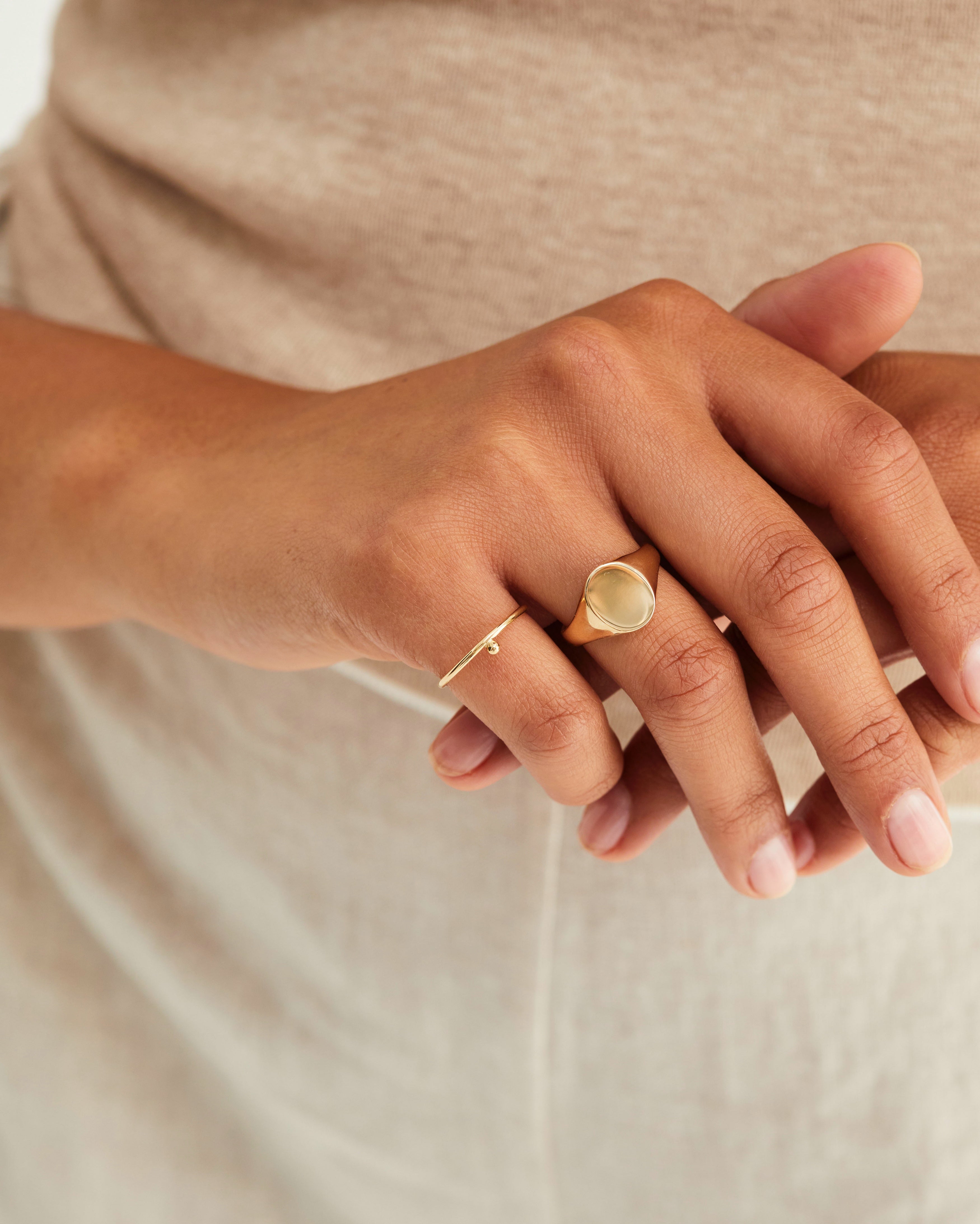 A hand adorned with the Arden Signet Ring and the Balance Ring, both in yellow gold.