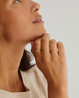 A woman's hand adorned in the Moon Ring and the Precious Initial Ring, both in yellow gold.