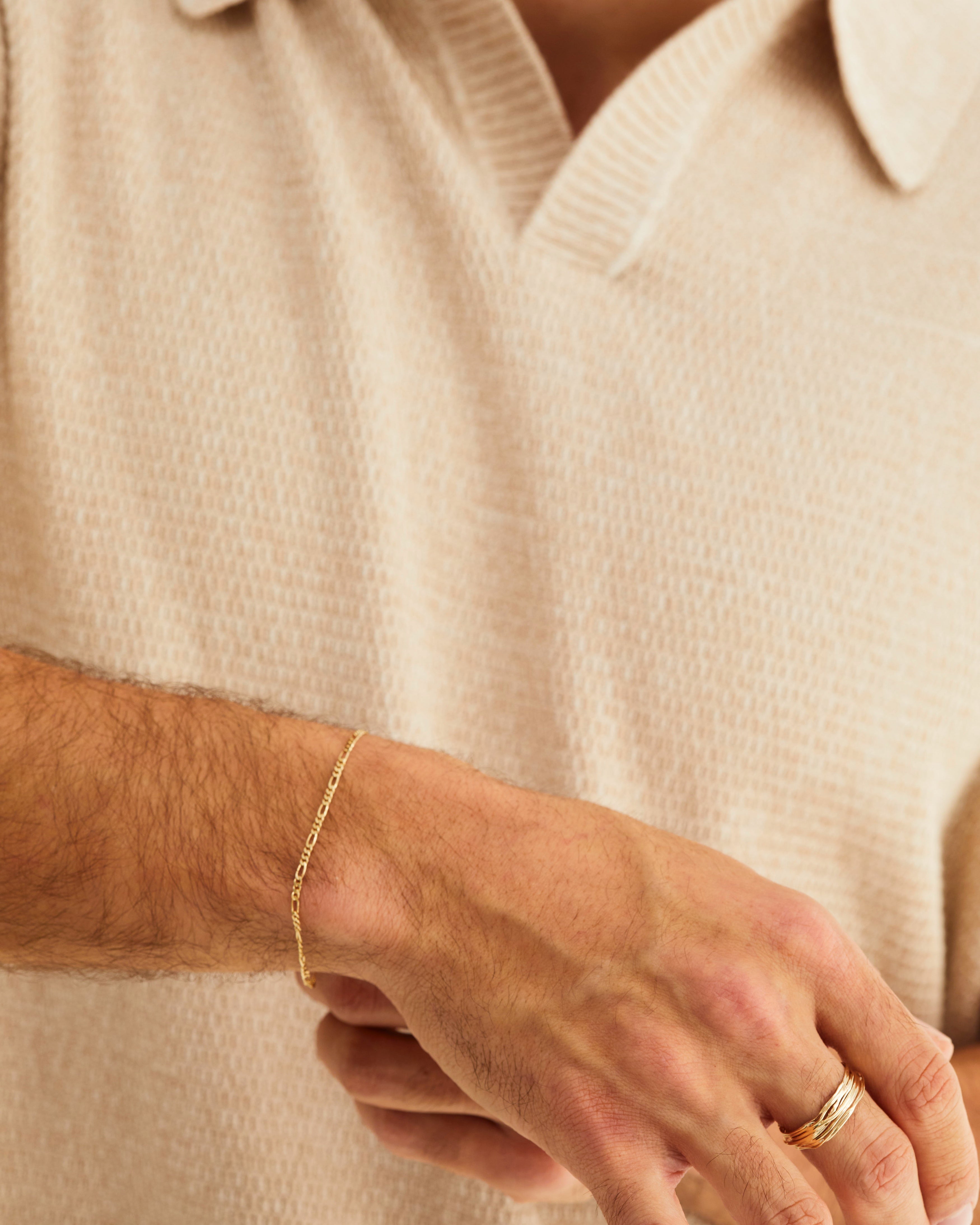 A male wears the bold Figaro chain bracelet in yellow gold