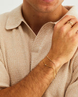 A man wears the Sonder Bracelet layered with a Figaro chain, in yellow gold