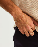 A man wears the Da Anam Bangle layered with a Figaro chain, in yellow gold
