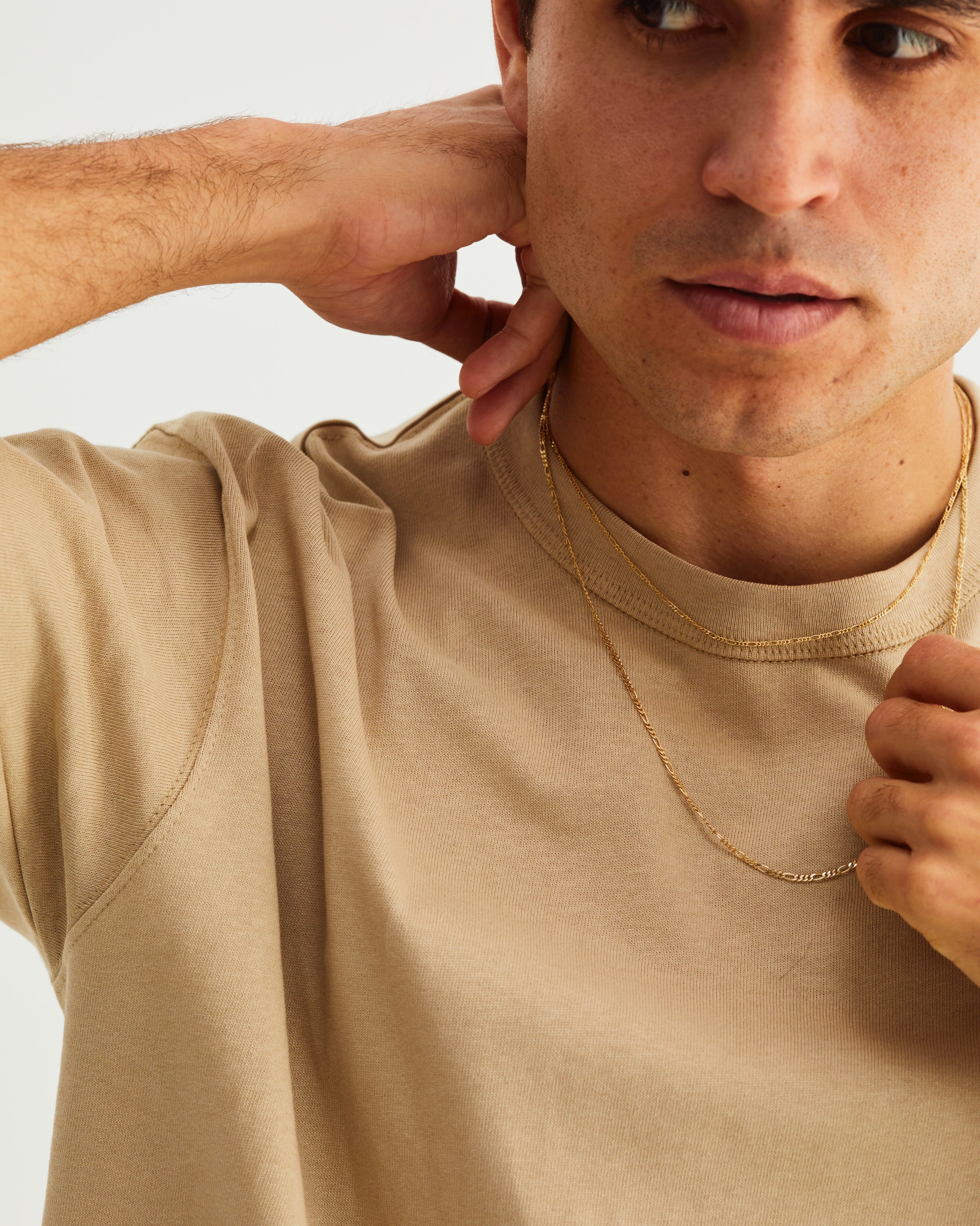 A man wears the fine Figaro chain necklace (shorter) layered with a bold Figaro chain necklace, both in yellow gold