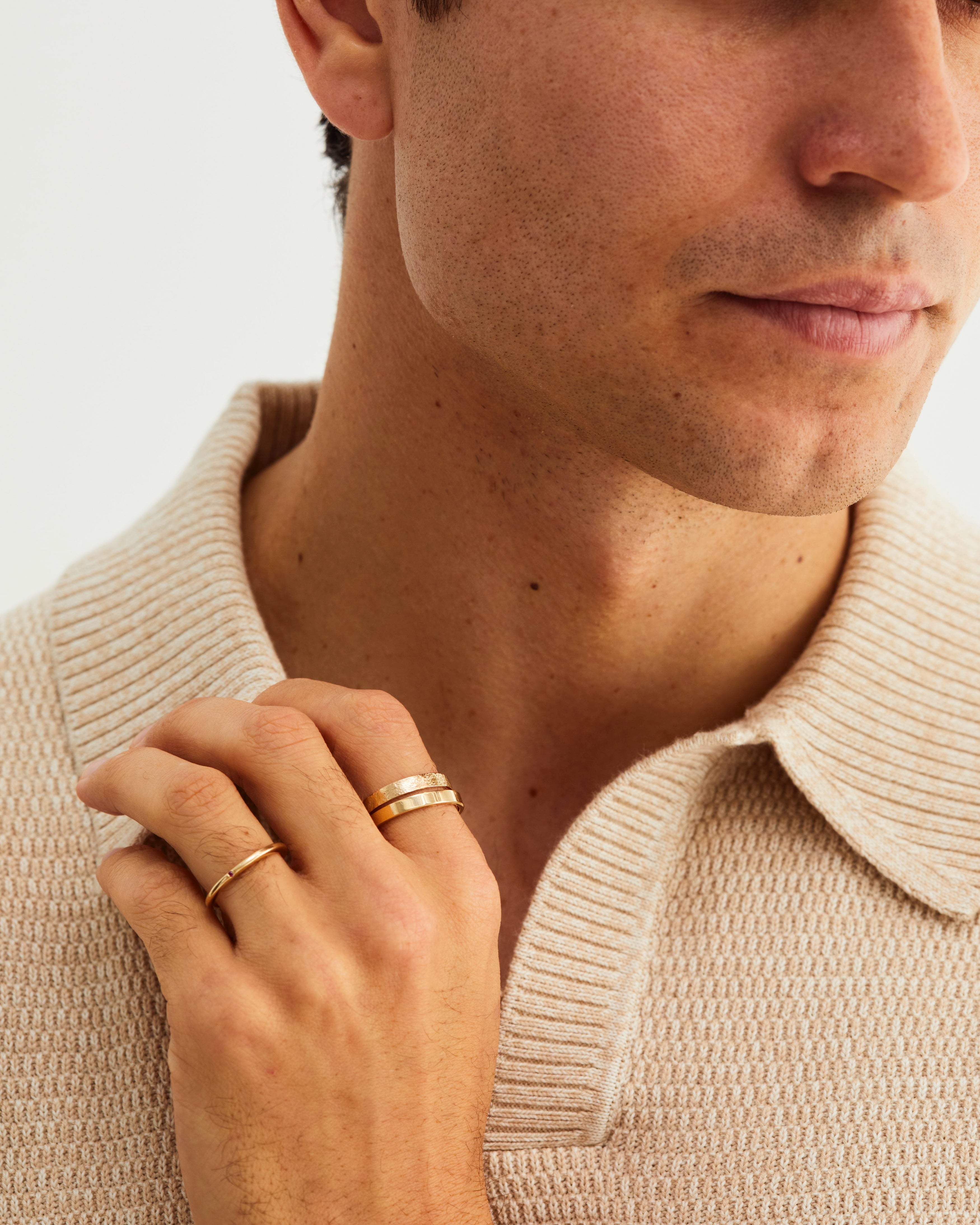A man wears our fine naum stacking ring with our squared wedding band, in yellow gold