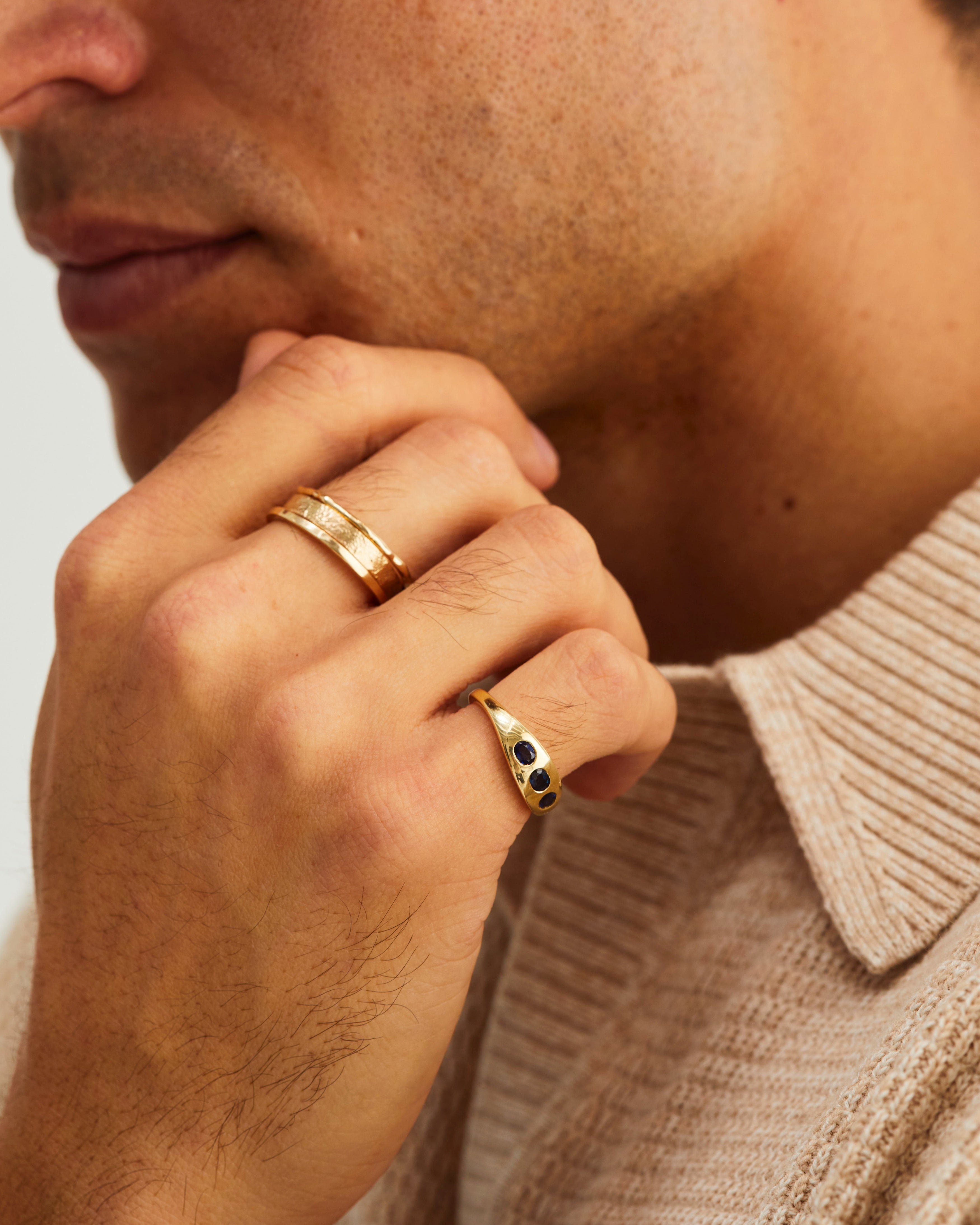 A man wears our Seule Trinity Ring with dark blue sapphires, and gold stacking rings