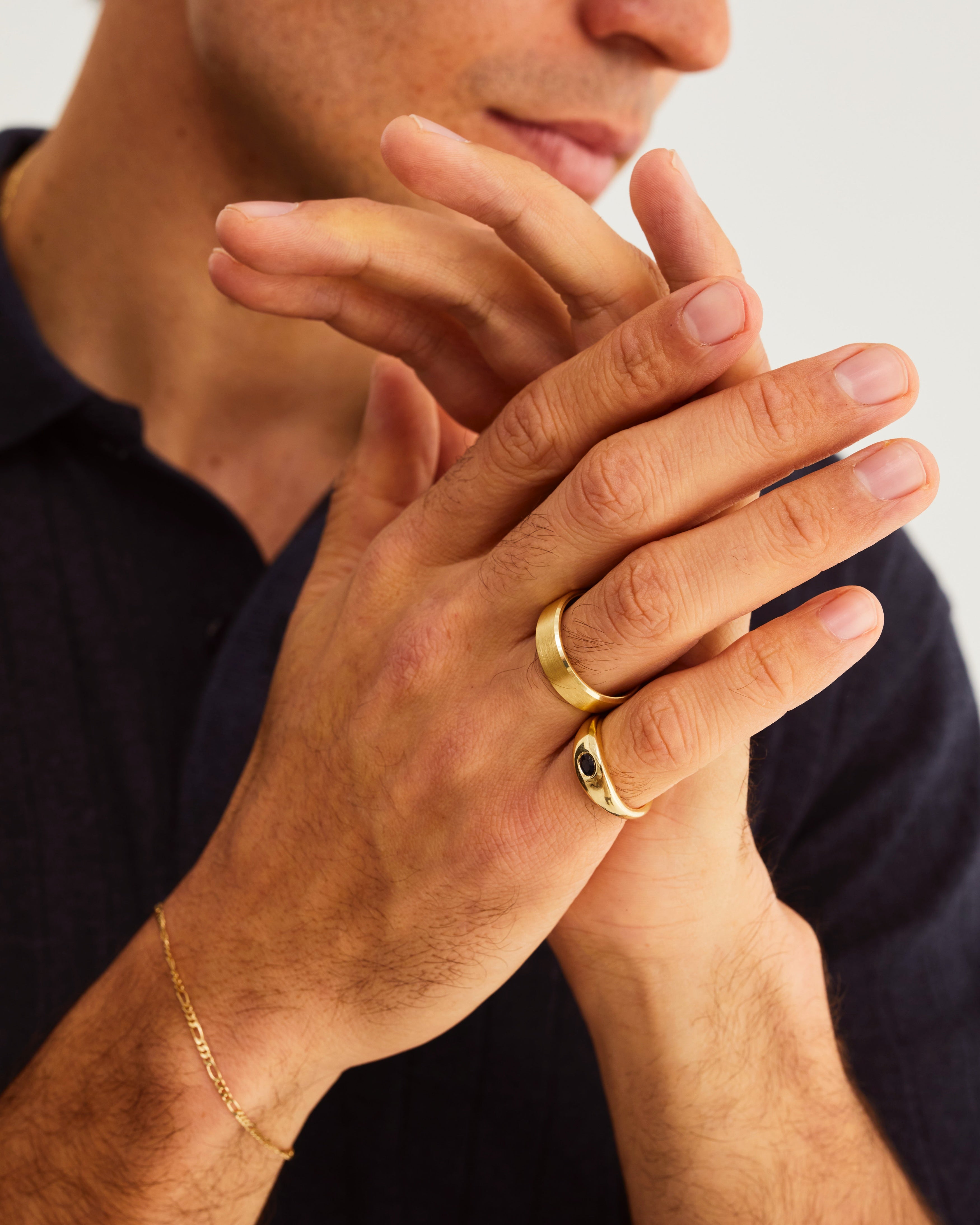 A man wears the Seule Single Ring with dark blue sapphires and bold wedding band in yellow gold