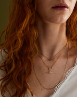 A woman wearing 3 layered necklaces, including the Terra Chain Necklace | Fine, Terra Chain Necklace | Bold and a Figaro Chain Necklace.