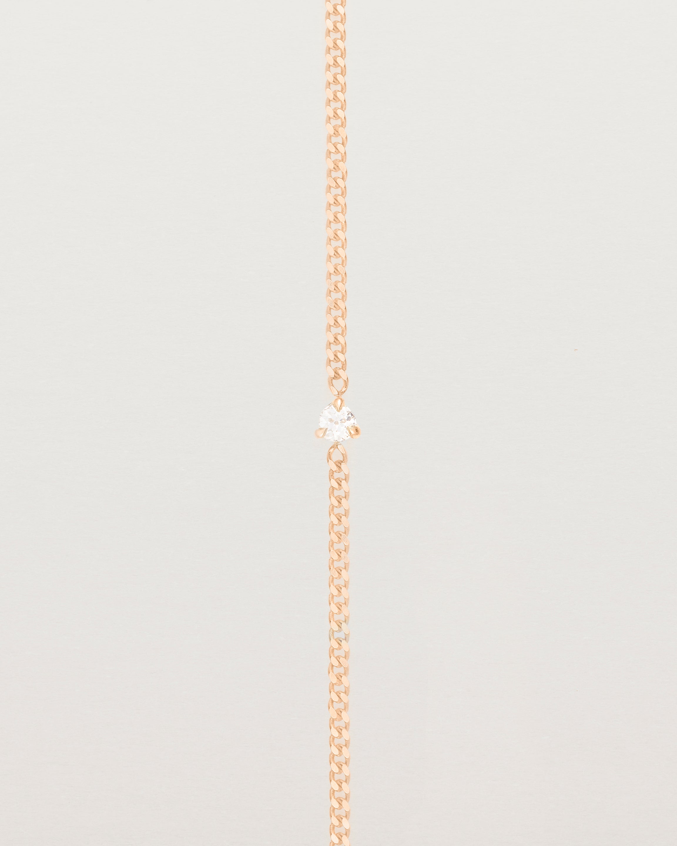 A rose gold chain bracelet featuring a single white old cut diamond