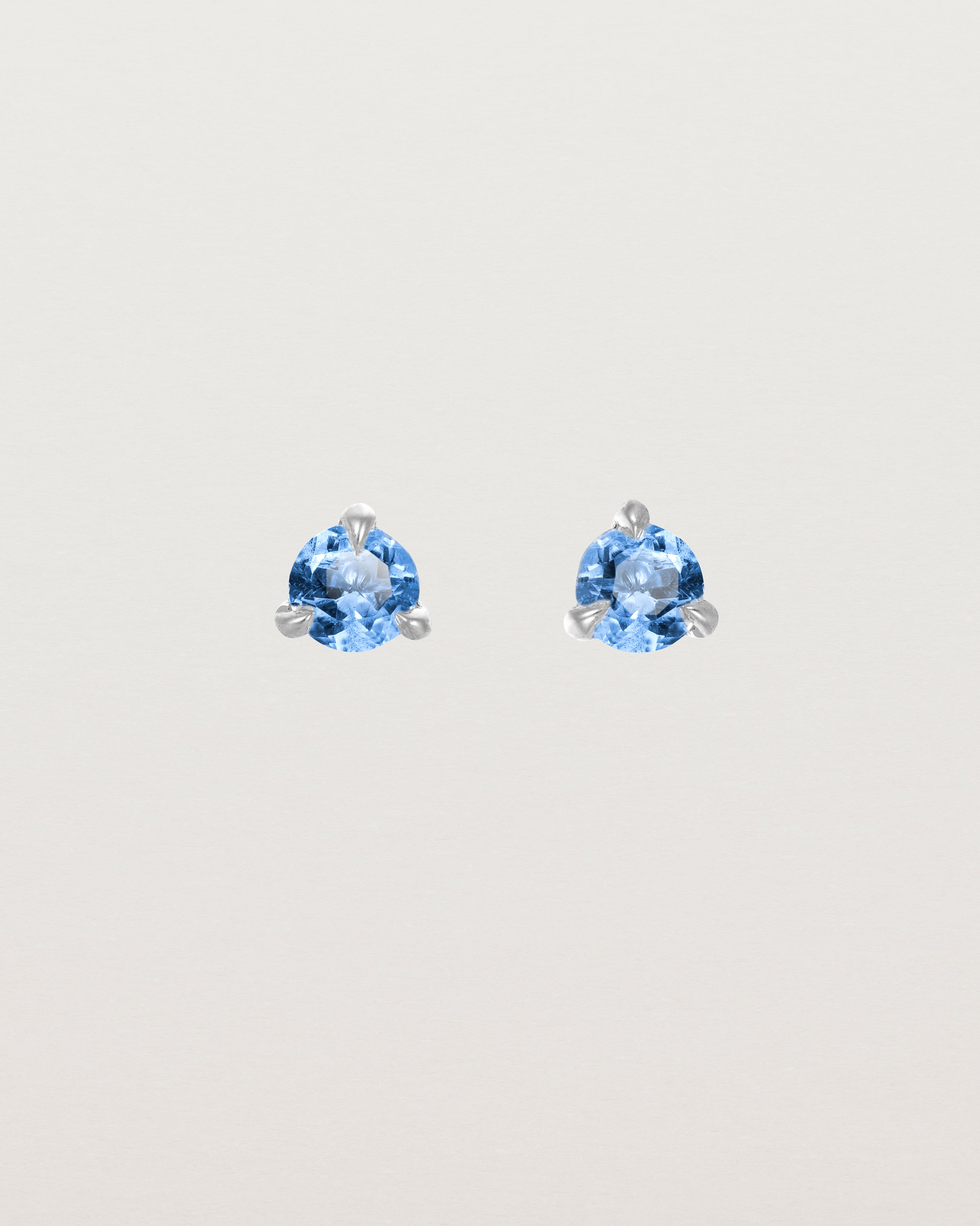 Front facing deep etched image of a pair of white gold earrings with a blue topaz birthstone.
