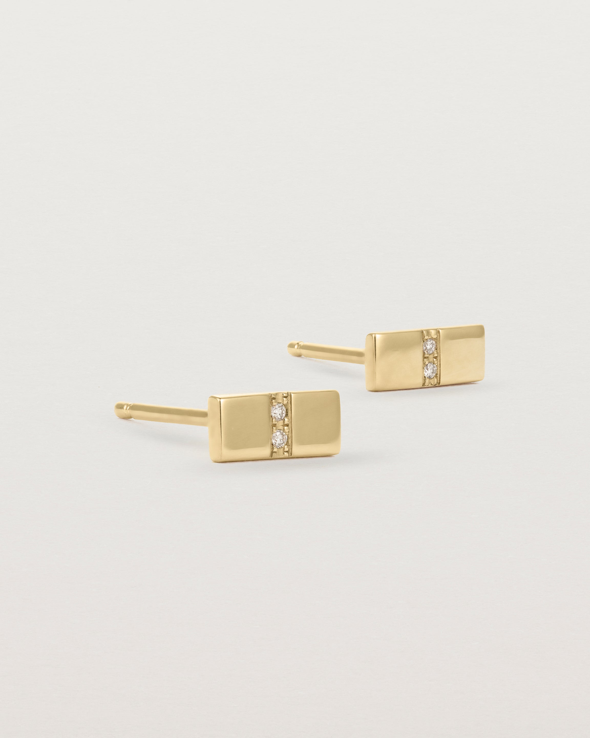 A pair of small yellow gold rectangle studs featuring two white diamonds set in the centre