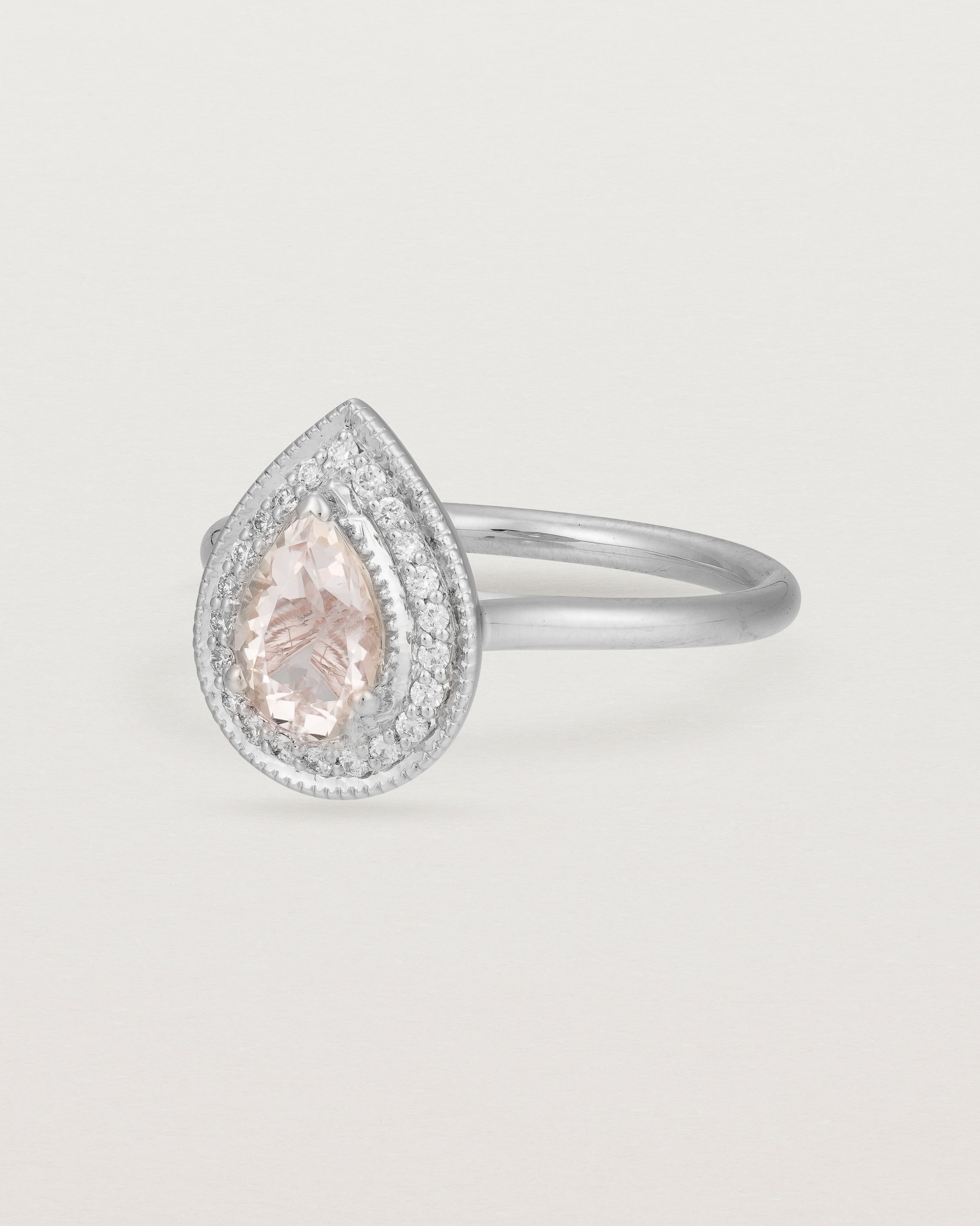 Side view pear halo ring featuring a pear cut pale pink morganite and a halo of white diamonds in white gold