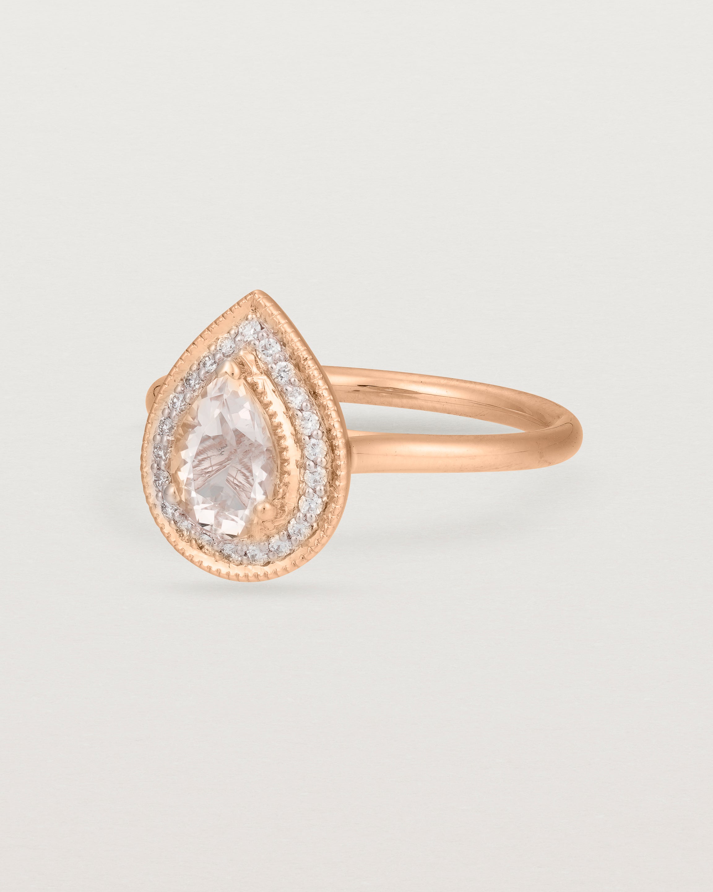 Side view pear halo ring featuring a pear cut pale pink morganite and a halo of white diamonds in rose gold
