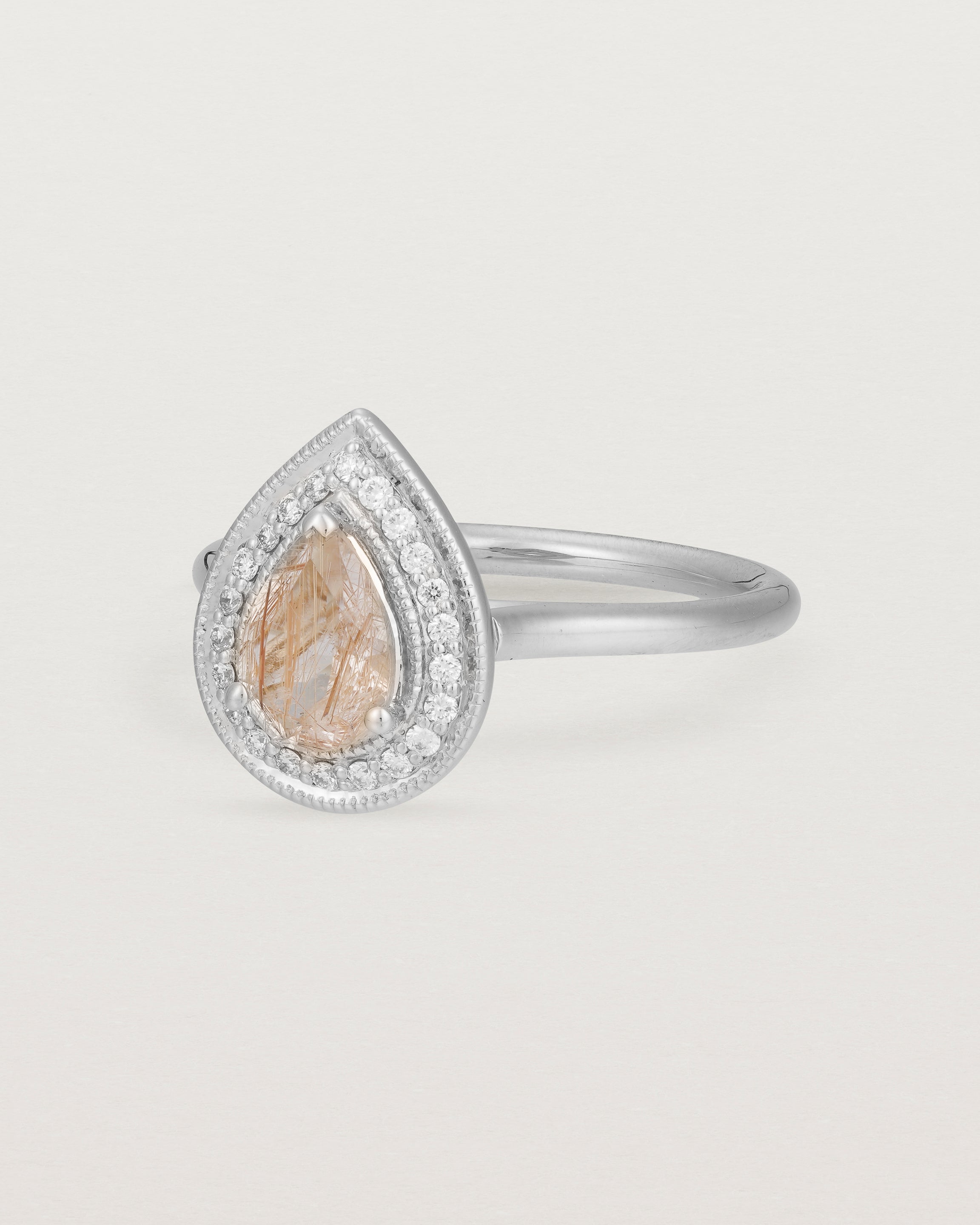 Side view pear halo ring featuring a pear cut rutilated quartz stone and a halo of white diamonds in white gold