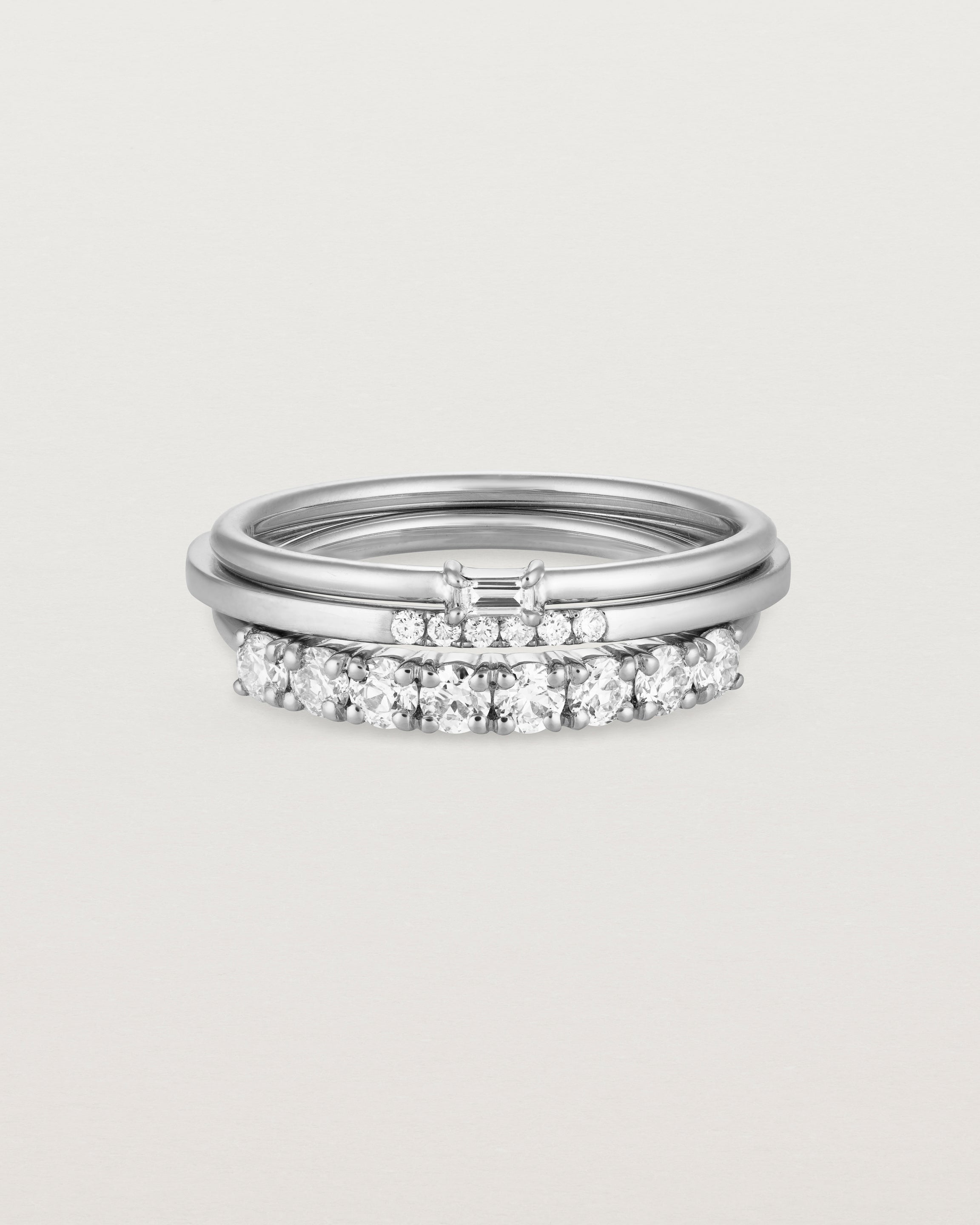 A set of three white gold bands, one featuring white round diamonds, one size white diamonds and one featuring a white emerald cut diamond