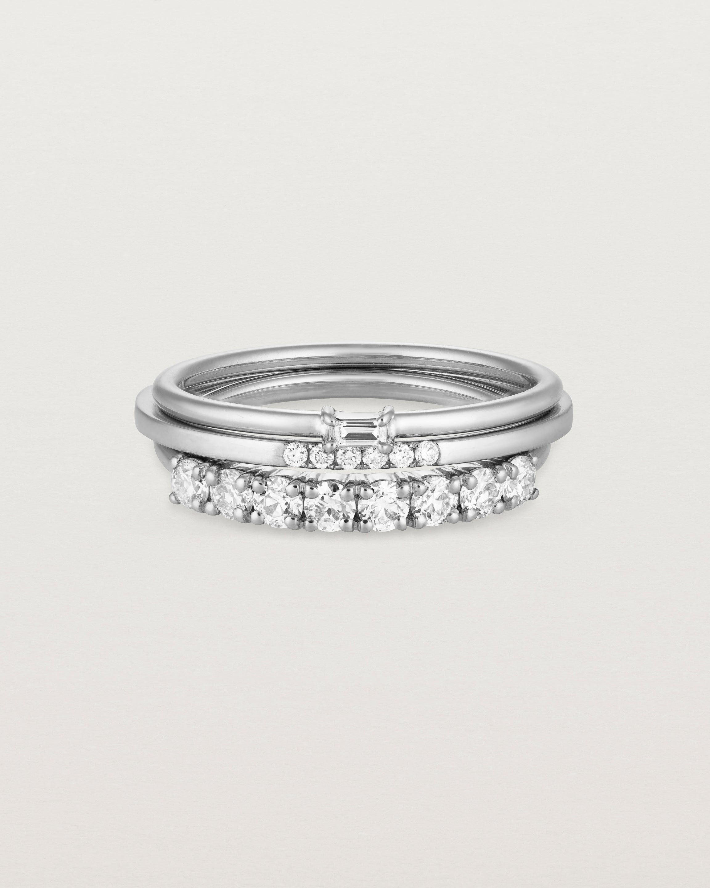 A set of three white gold bands, one featuring white round diamonds, one size white diamonds and one featuring a white emerald cut diamond