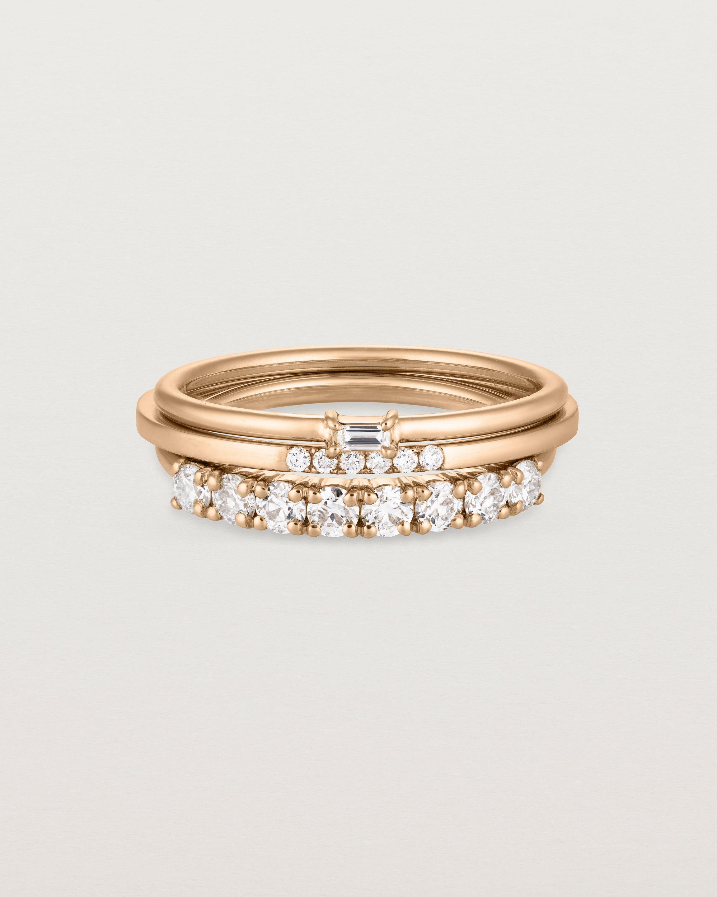 A set of three rose gold bands, one featuring white round diamonds, one size white diamonds and one featuring a white emerald cut diamond