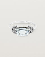 A white oval sapphire set east to west, adorned with clusters of white diamonds either side, and crafted in white gold