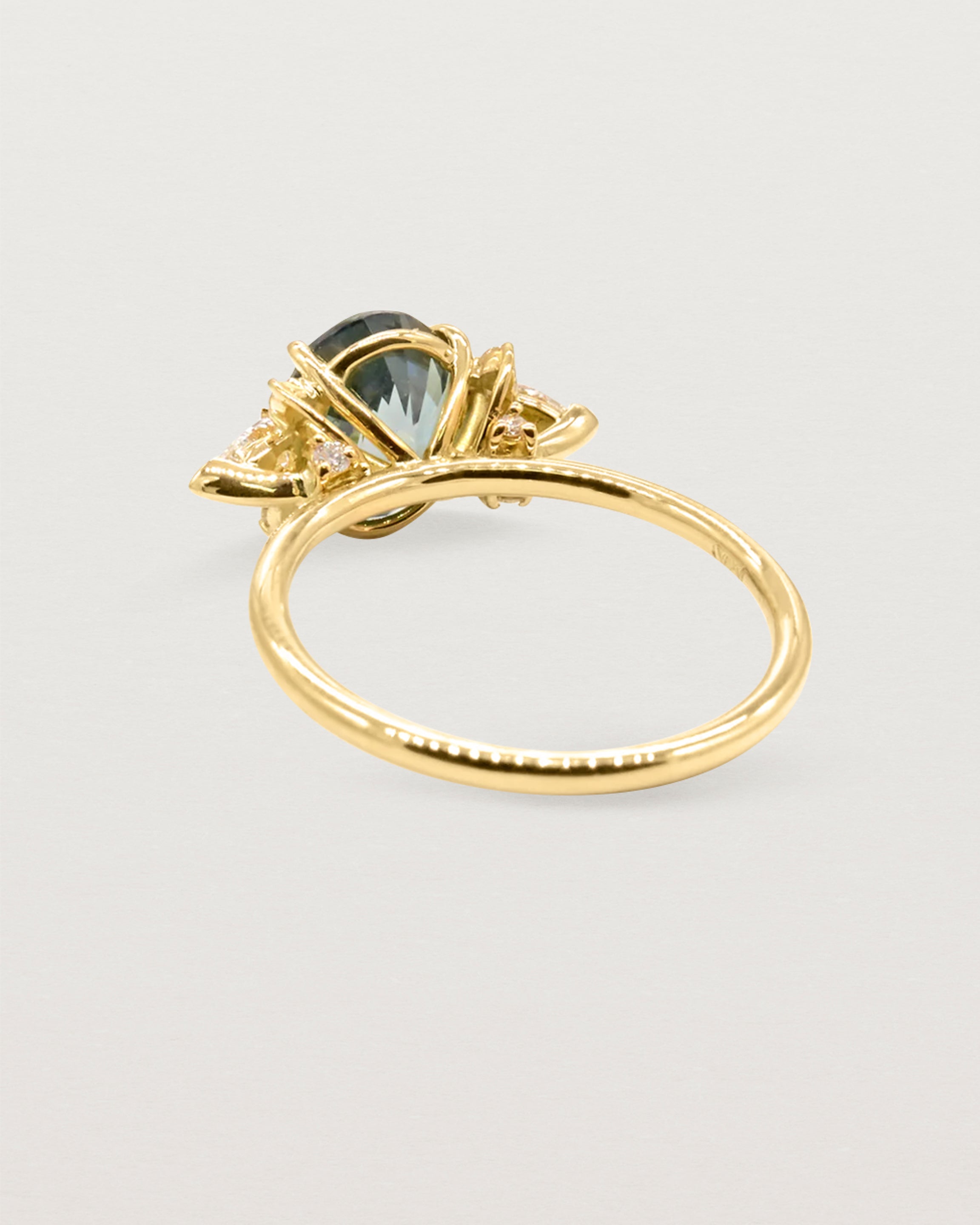 Back view of a  large oval teal sapphire adorned with white diamond clusters, crafted in yellow gold