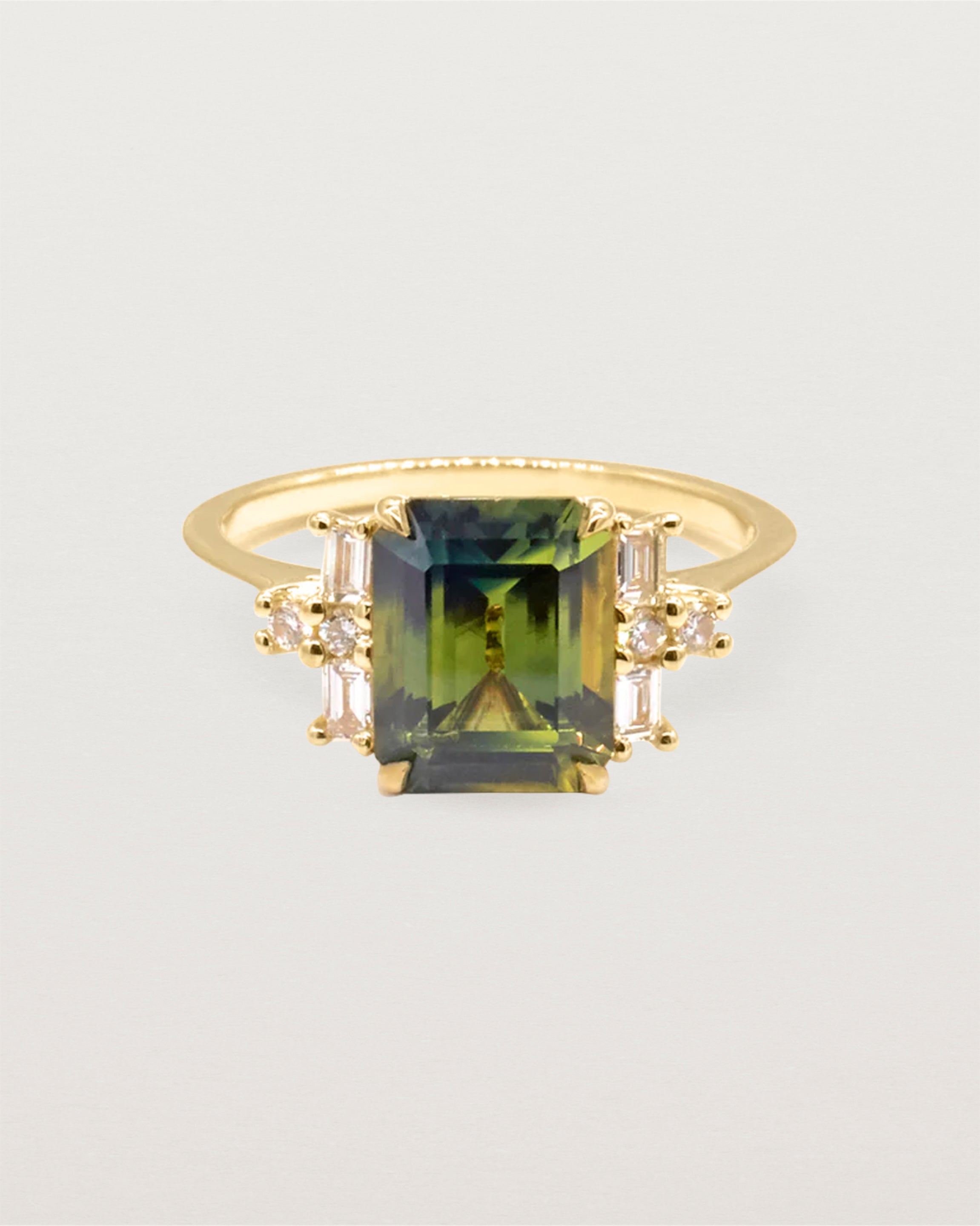A teal pear sapphire is framed by a cluster of two baguettes and round diamonds on either side, crafted in yellow gold
