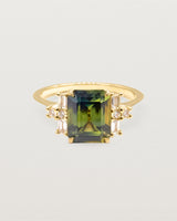 A teal pear sapphire is framed by a cluster of two baguettes and round diamonds on either side, crafted in yellow gold