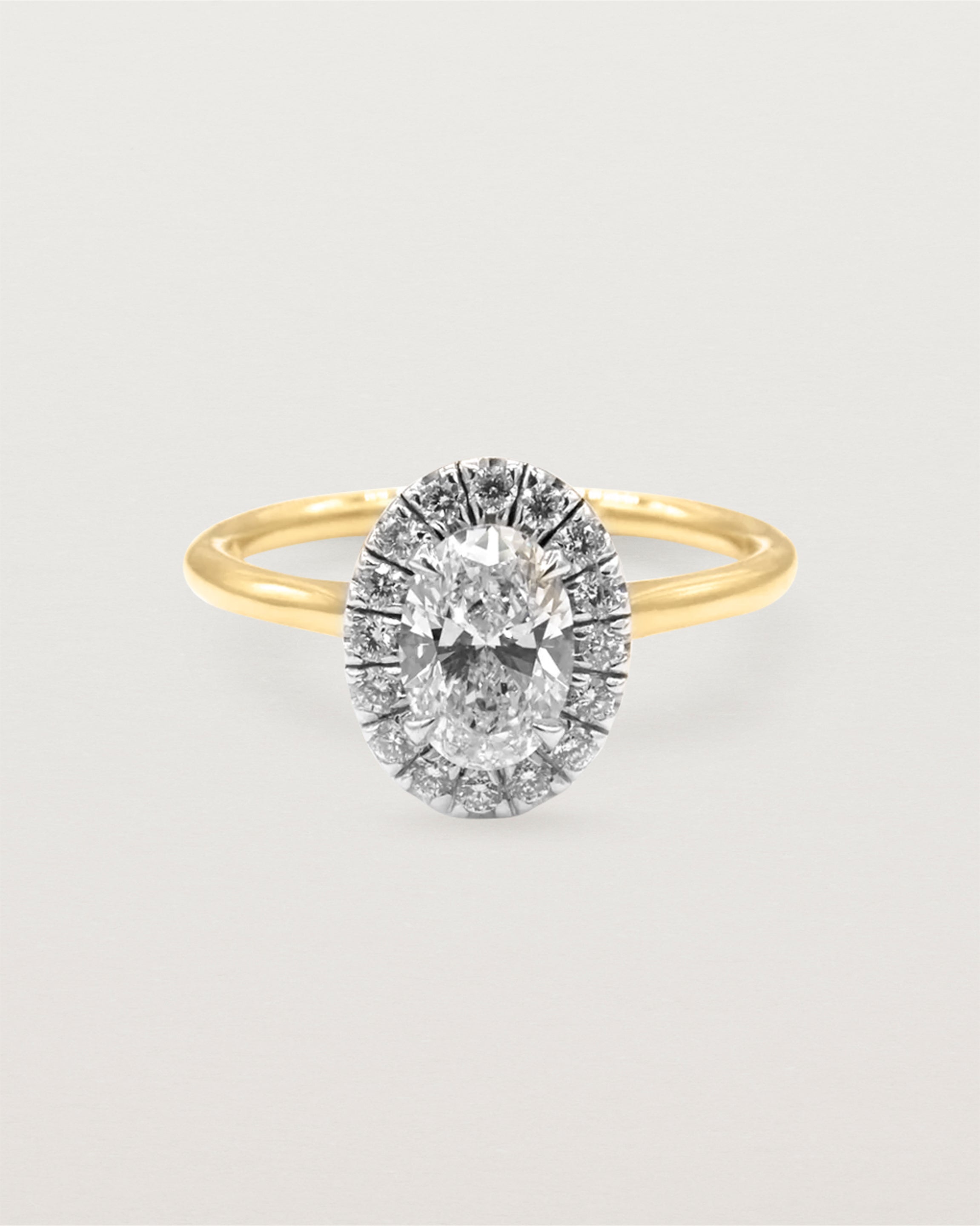 A 0.70ct oval cut diamond is adorned with a sparkling white diamond halo crafted in both yellow gold and white gold 