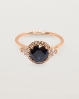 A round cut parti sapphire surrounded by a halo of white diamonds and crafted in rose gold
