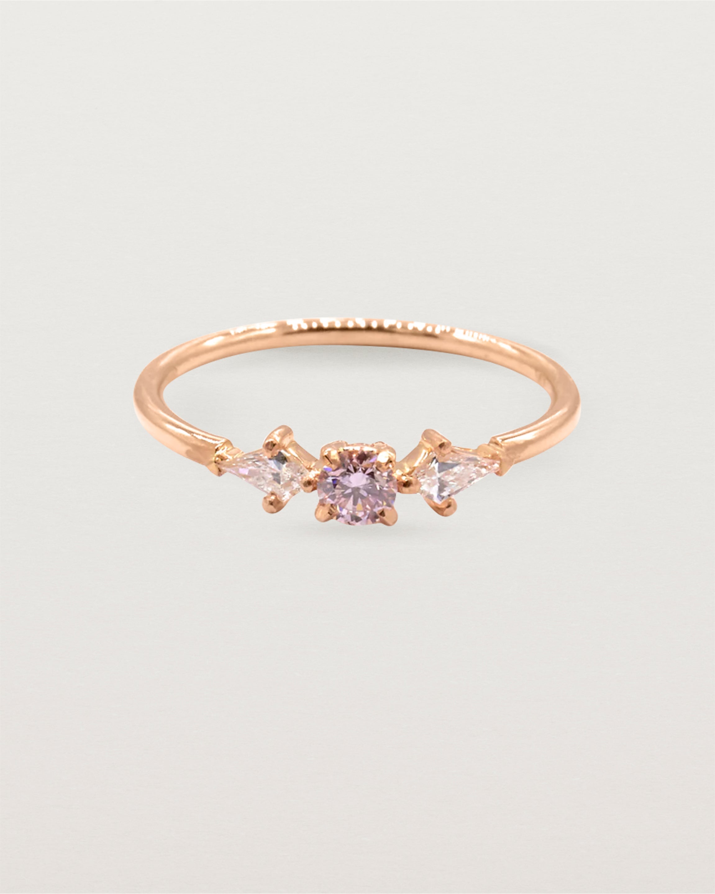 A blush-toned, certified Argyle pink diamond sits between two bright white kite shaped diamonds on a fine round band.