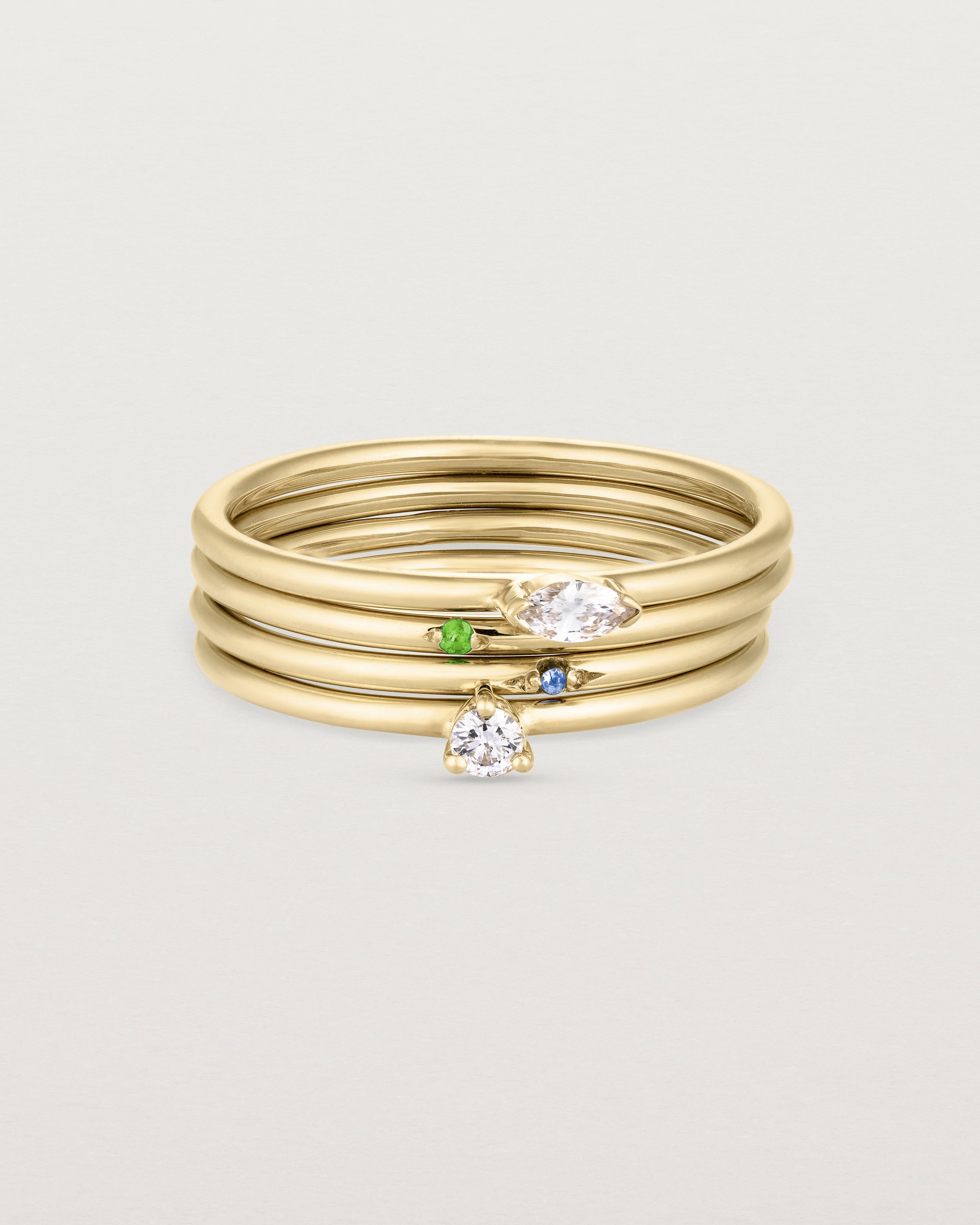 A set of four yellow gold rings, featuring white diamonds and blue sapphire and an emerald.