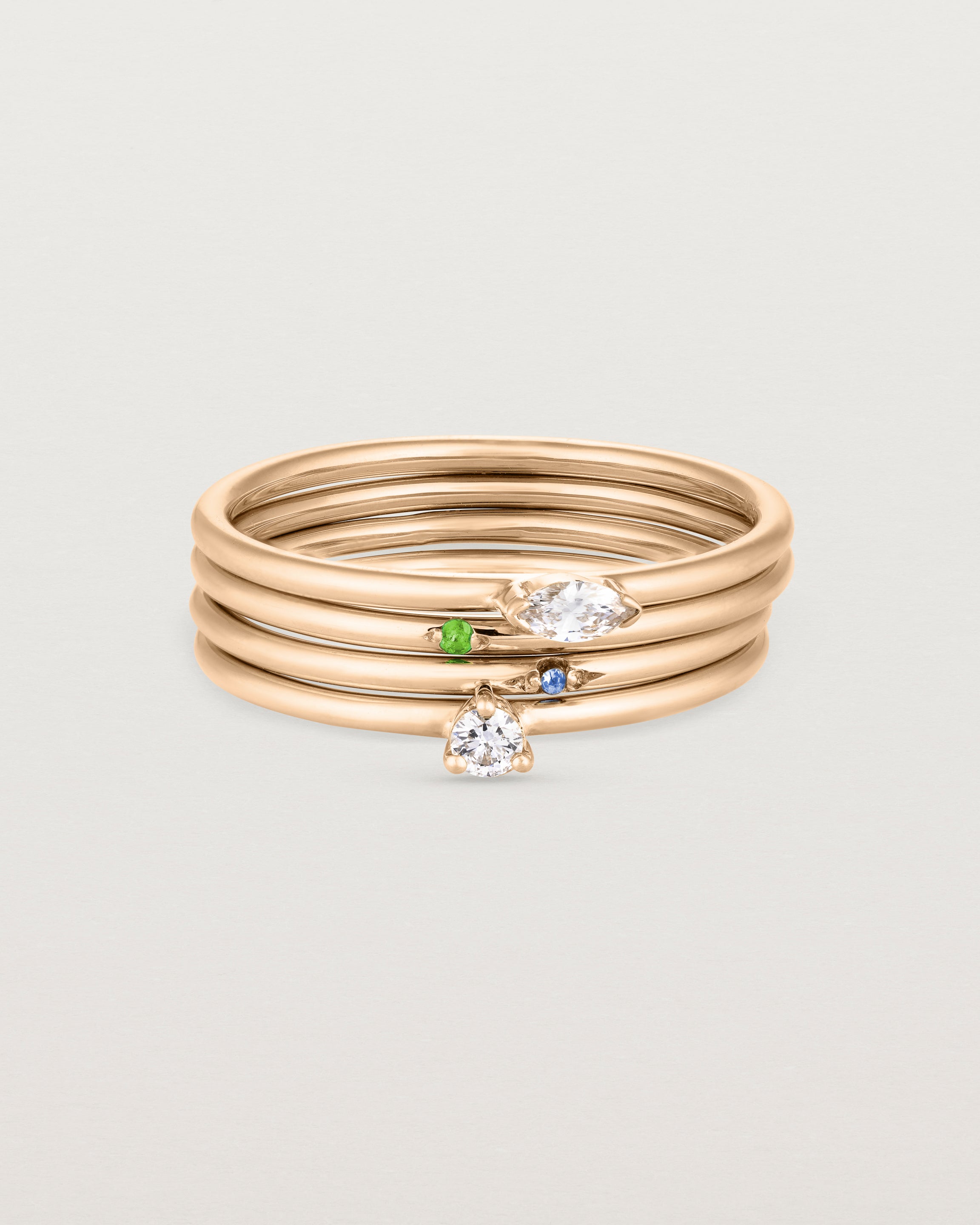 A set of four rose gold rings, featuring white diamonds and blue sapphire and an emerald.
