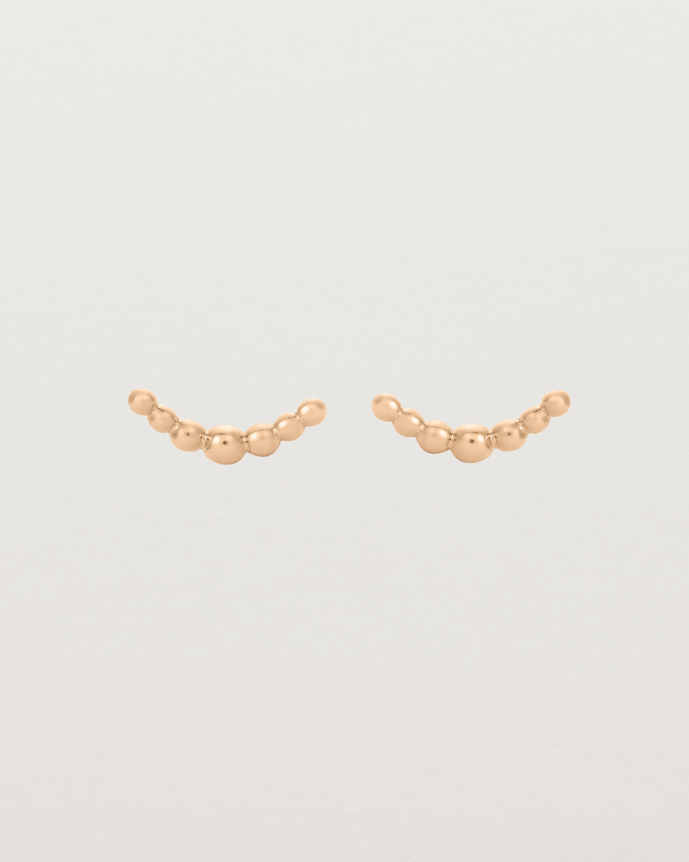 A pair of rose gold studs featuring an arc of round metal balls