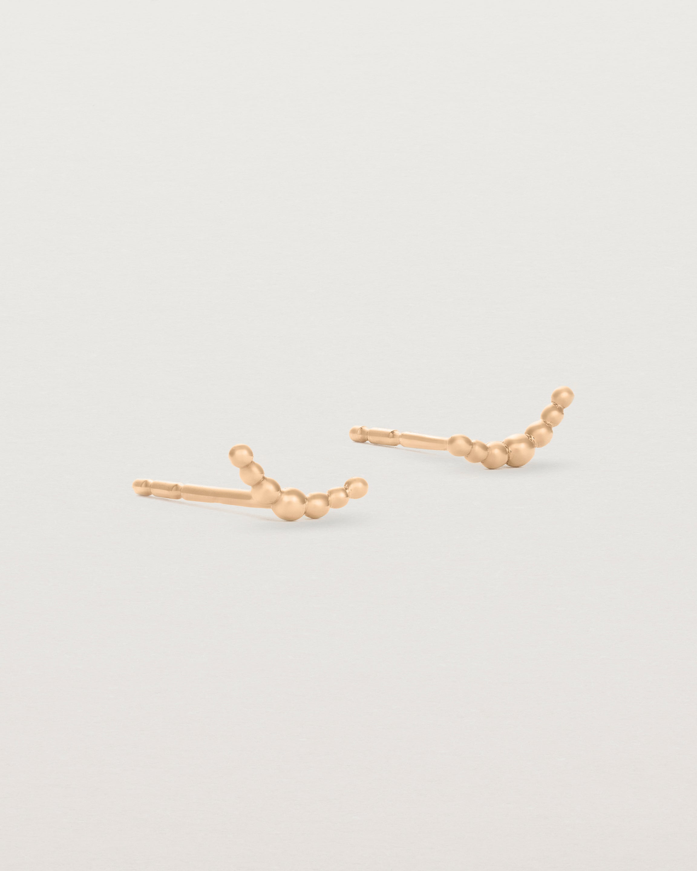 A pair of rose gold studs featuring an arc of round metal balls