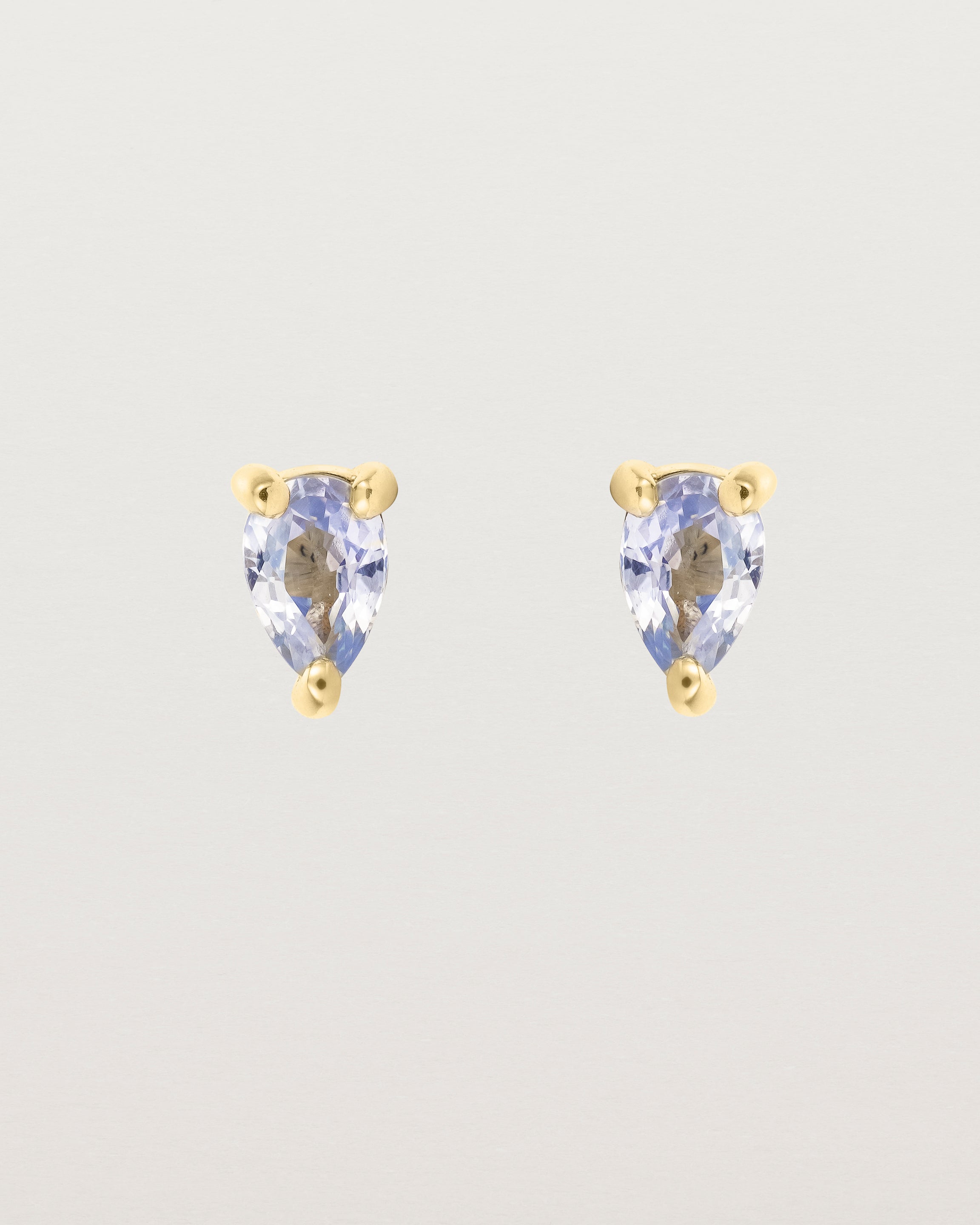 A pair of yellow gold studs featuring a pear cut pale blue sapphire