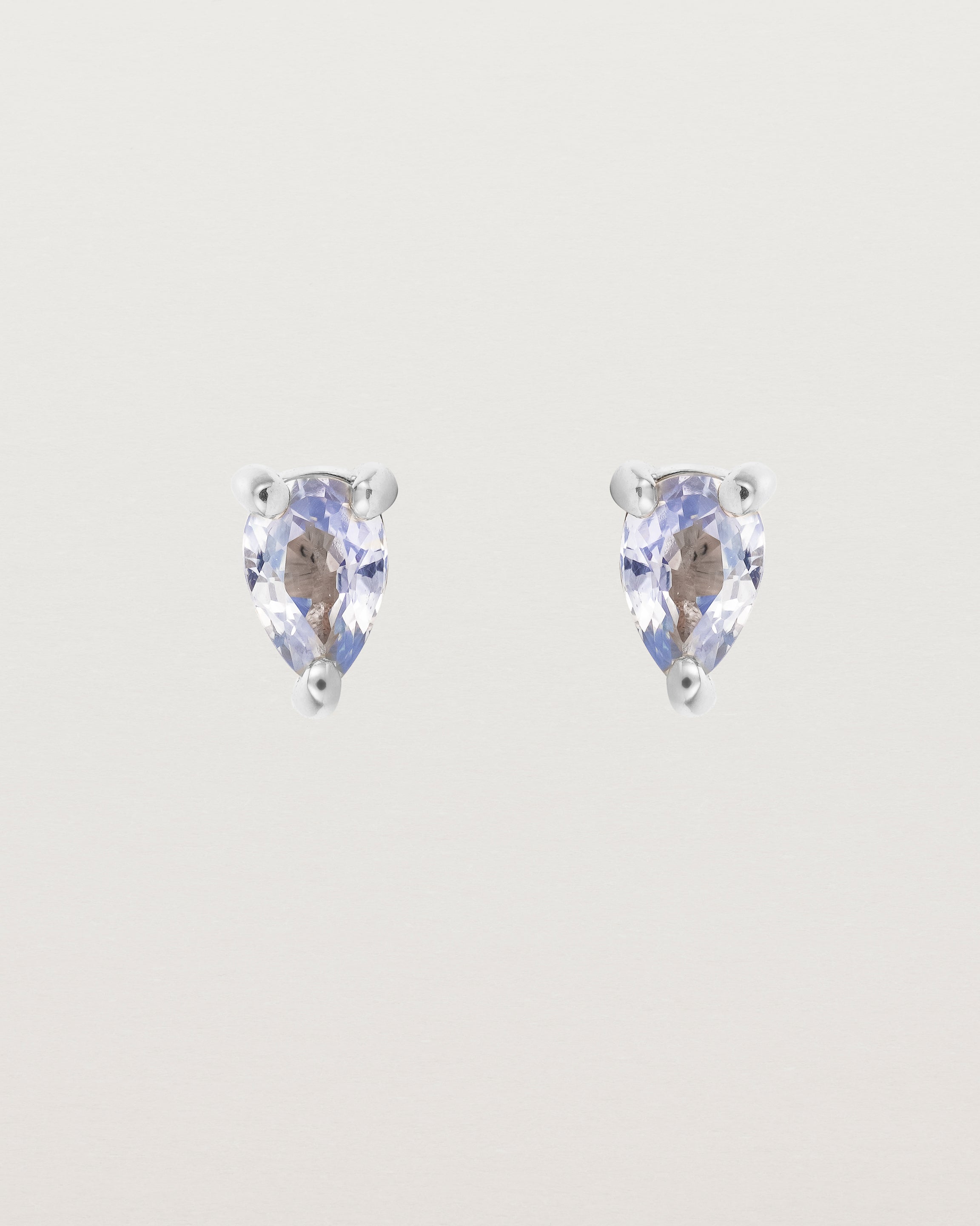 A pair of white gold studs featuring a pear cut pale blue sapphire