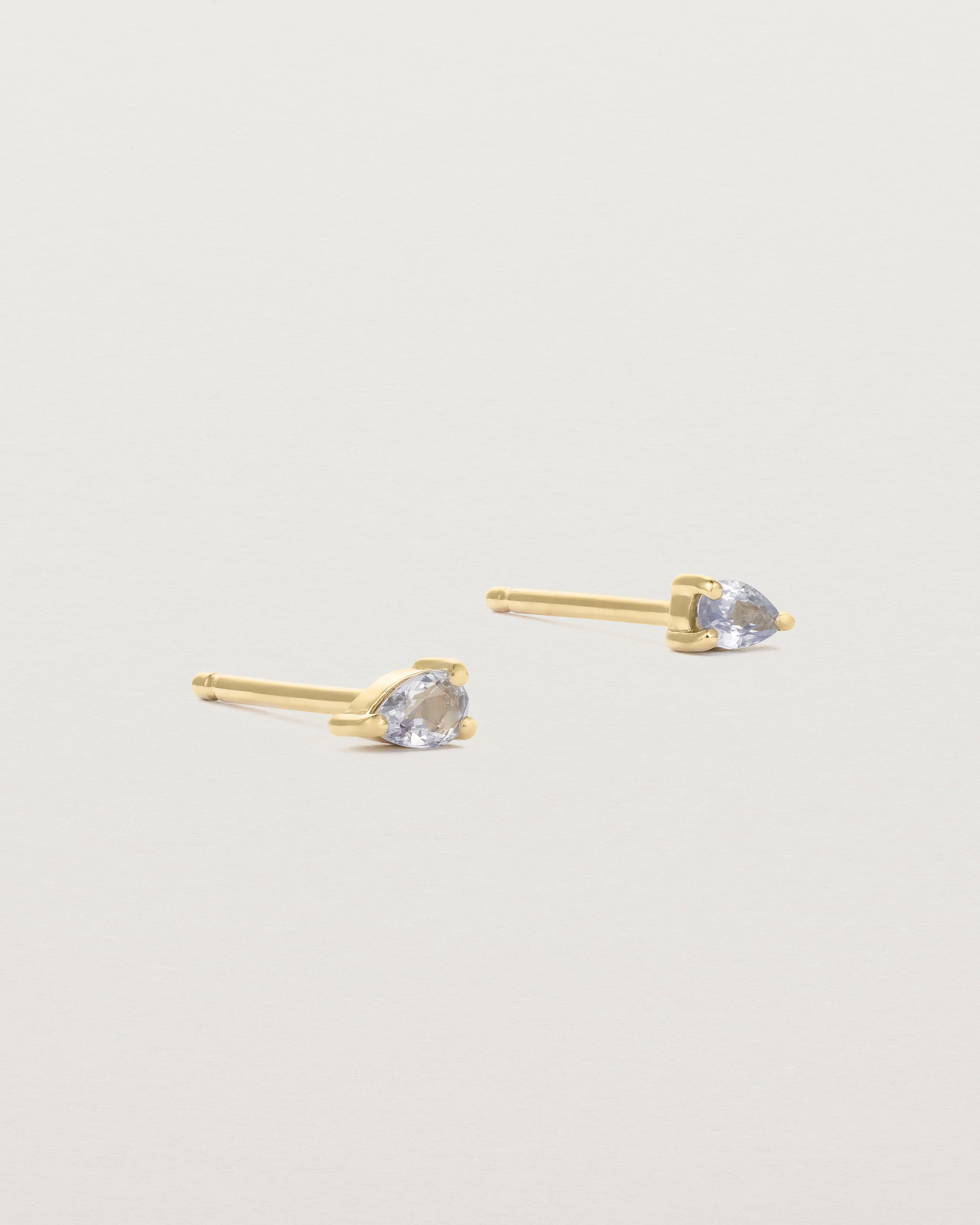 A pair of yellow gold studs featuring a pear cut pale blue sapphire