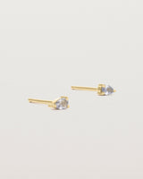 A pair of yellow gold studs featuring a pear cut pale blue sapphire