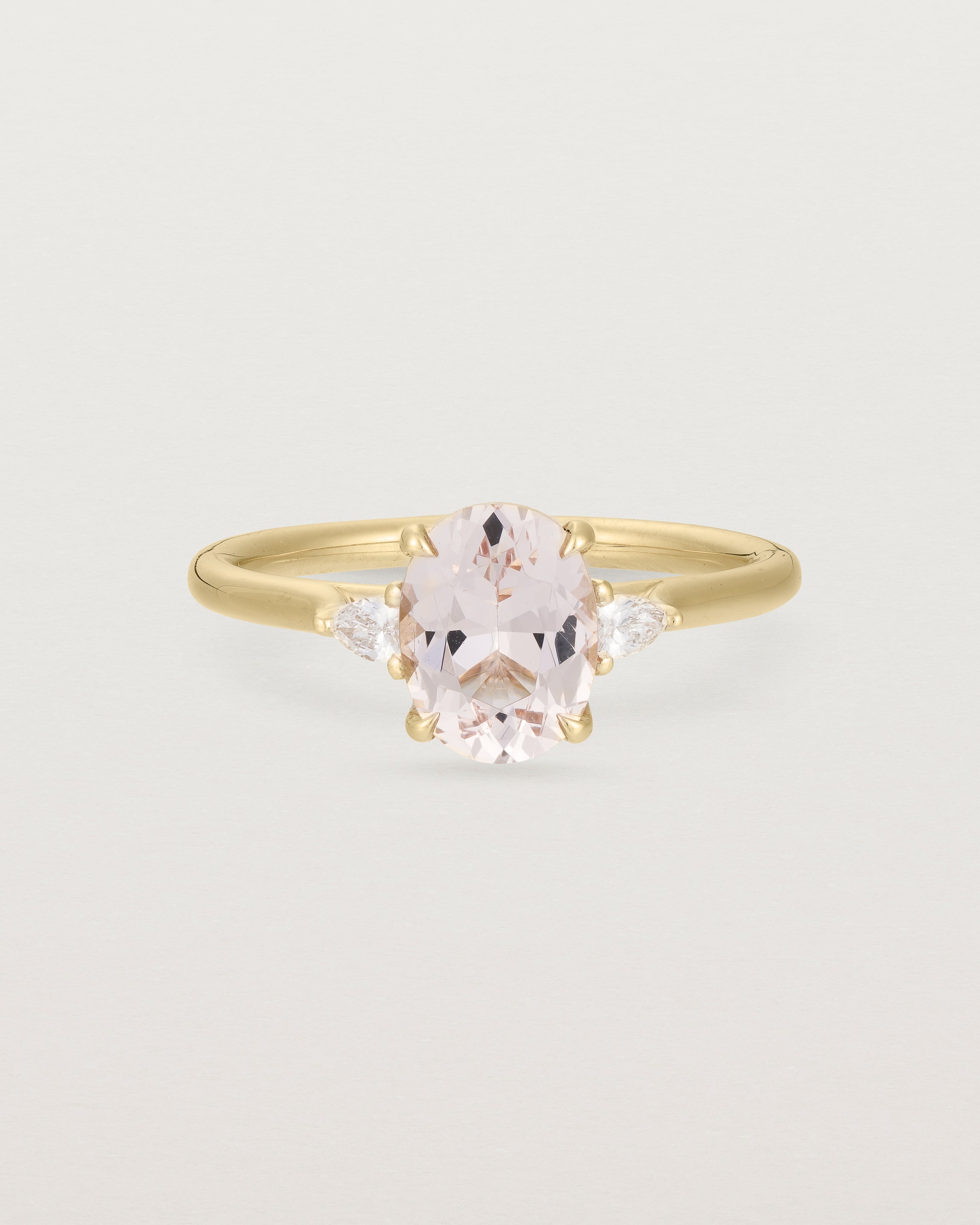An oval morganite adorned with white diamonds either side, featuring a sweeping setting and crafted in yellow gold