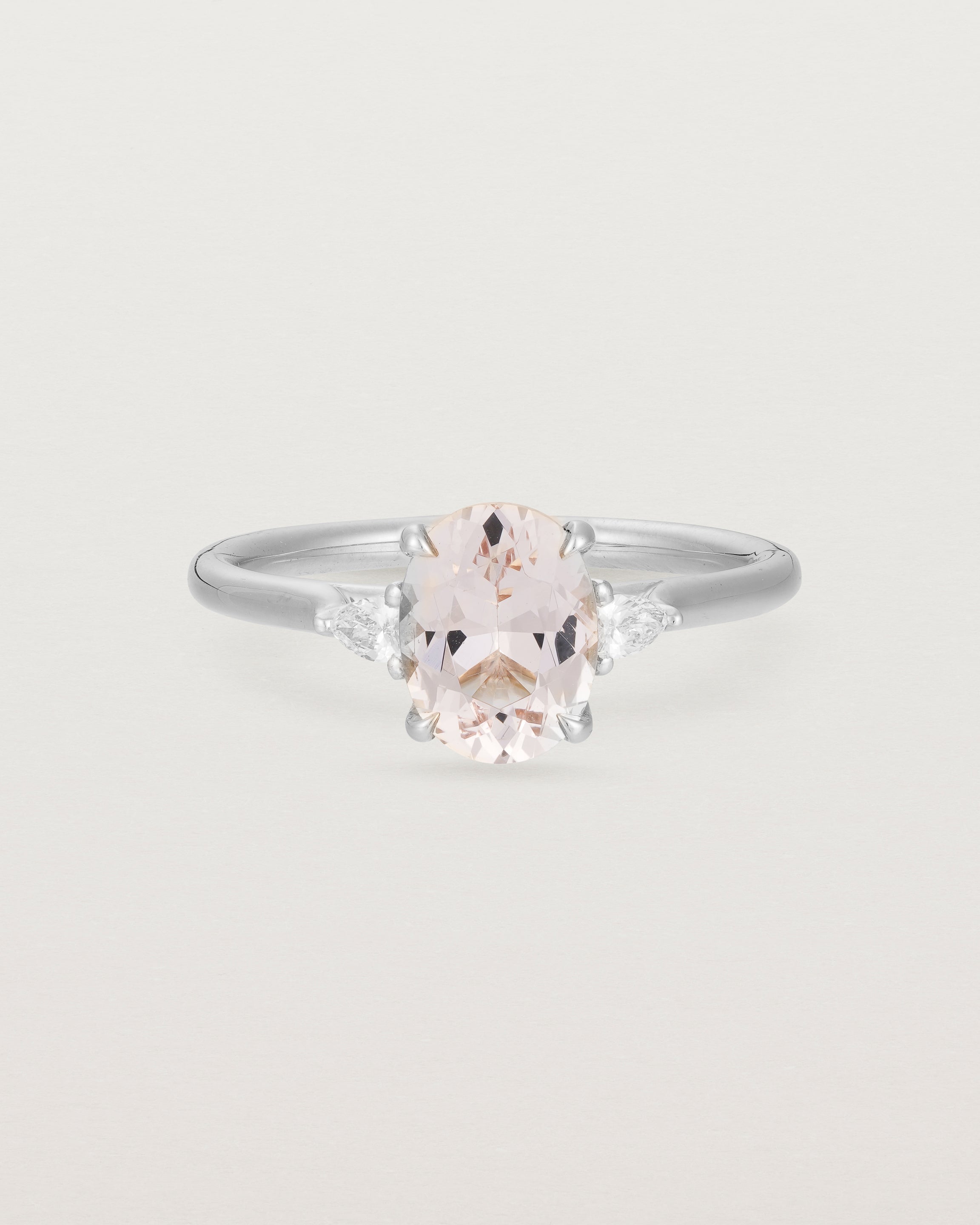An oval morganite adorned with two white diamonds either side, featuring a sweeping setting and crafted in white gold